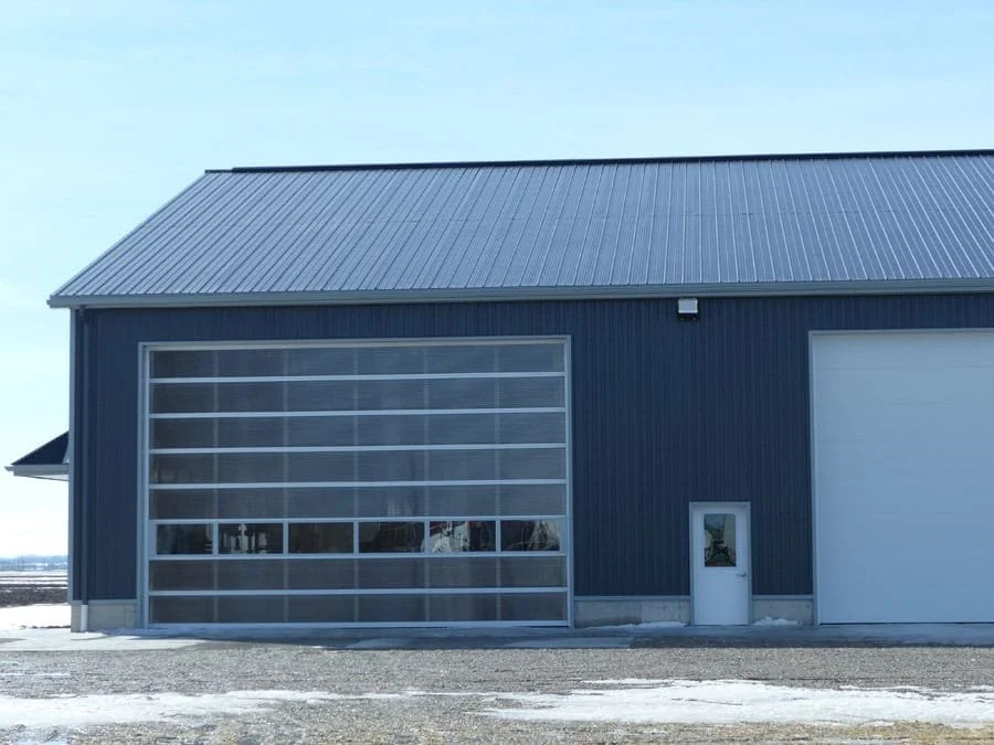 Exterior of a modern blue garage with a large glass door and a smaller white door, on a sunny day.