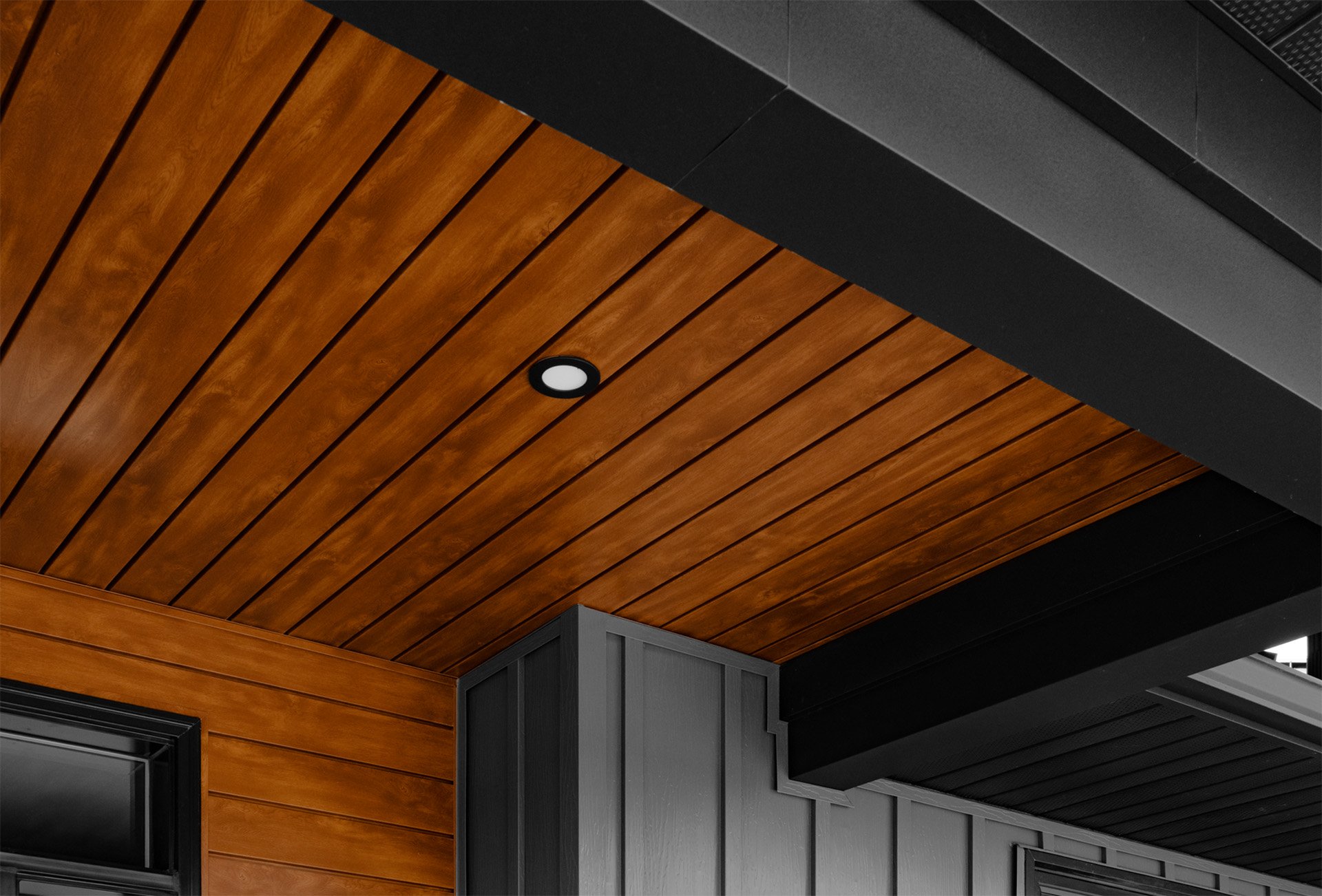 Close-up of a ceiling with wooden paneling and black accents, including a ceiling vent and a round recessed light.