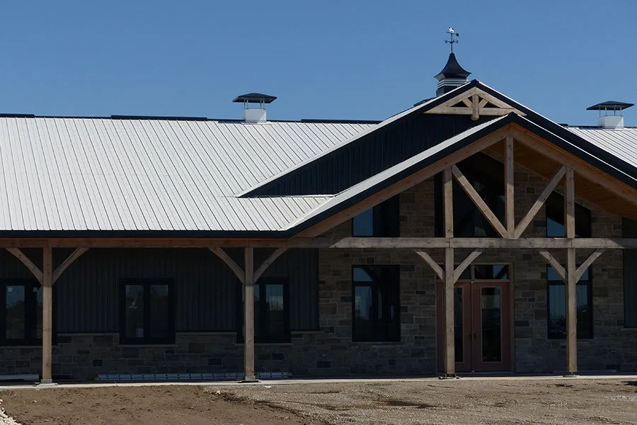 A new building with a pitched metal roof, wooden beams, and brick walls, under a clear blue sky.