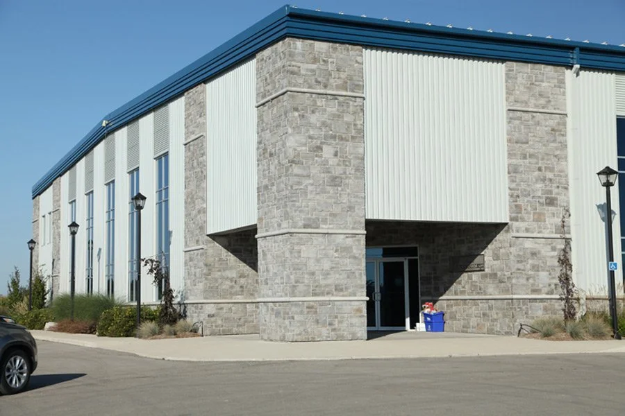 Exterior view of a commercial or industrial building with stone and metal siding, multiple windows, and several street lamps in front.