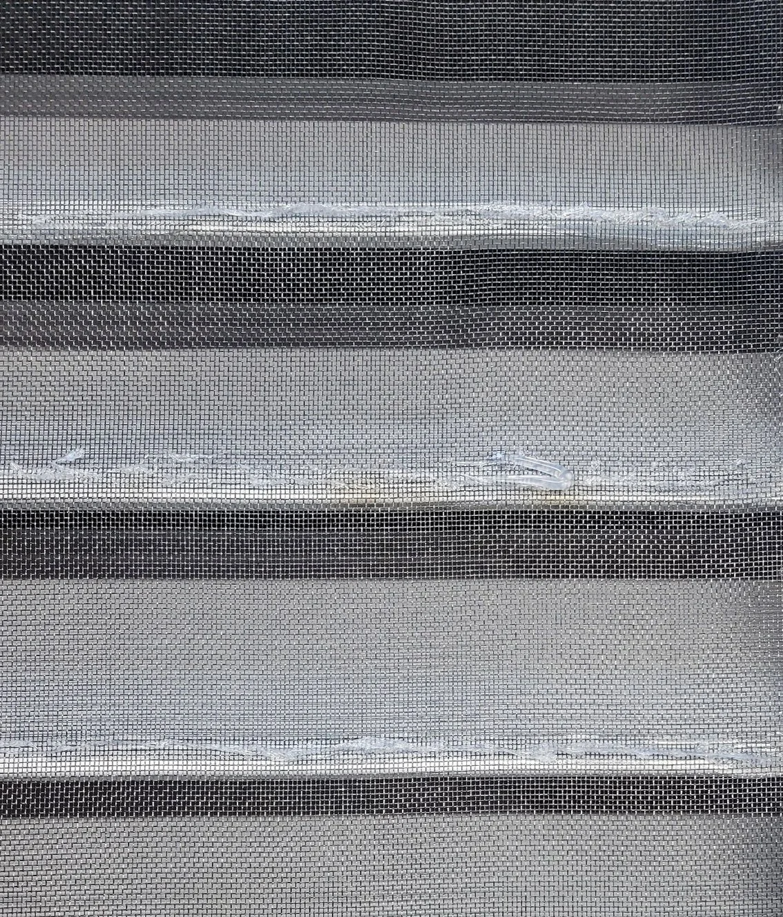 Close-up of a window screen with horizontal black and white stripes behind it.