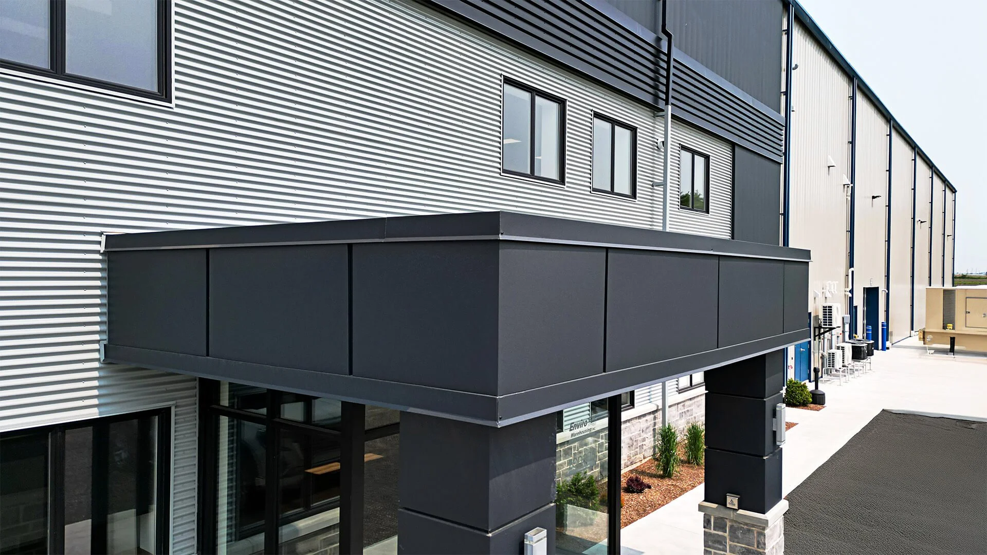 Modern industrial building with metal siding, windows, and a black balcony or overhang.