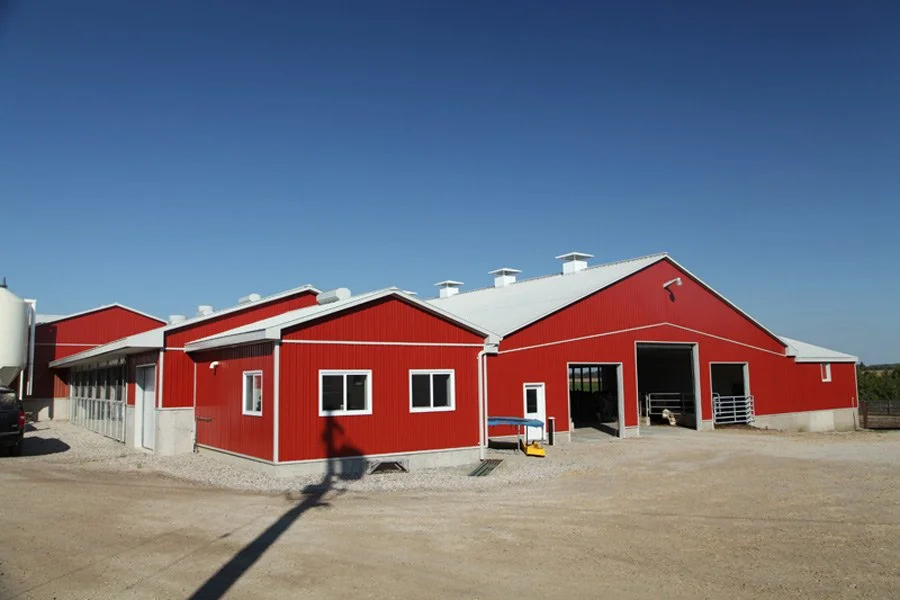 Red barn with white roof and trim, multiple large doors open to a dirt yard, clear blue sky.
