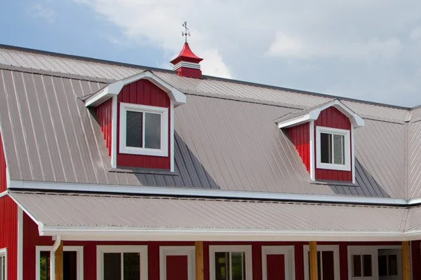 Close-up of a red farmhouse roof with two dormer windows and a weather vane on top of a small tower.