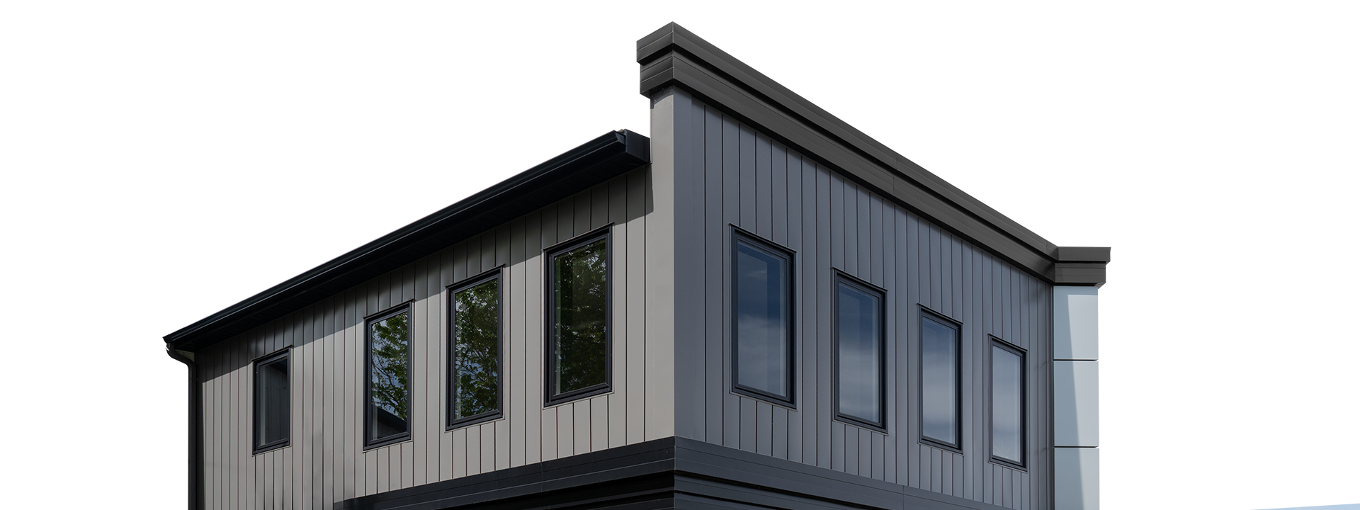 Close-up of a modern house's corner with metal siding and five rectangular windows with black frames, reflecting trees and sky, against a background of a clear blue sky.