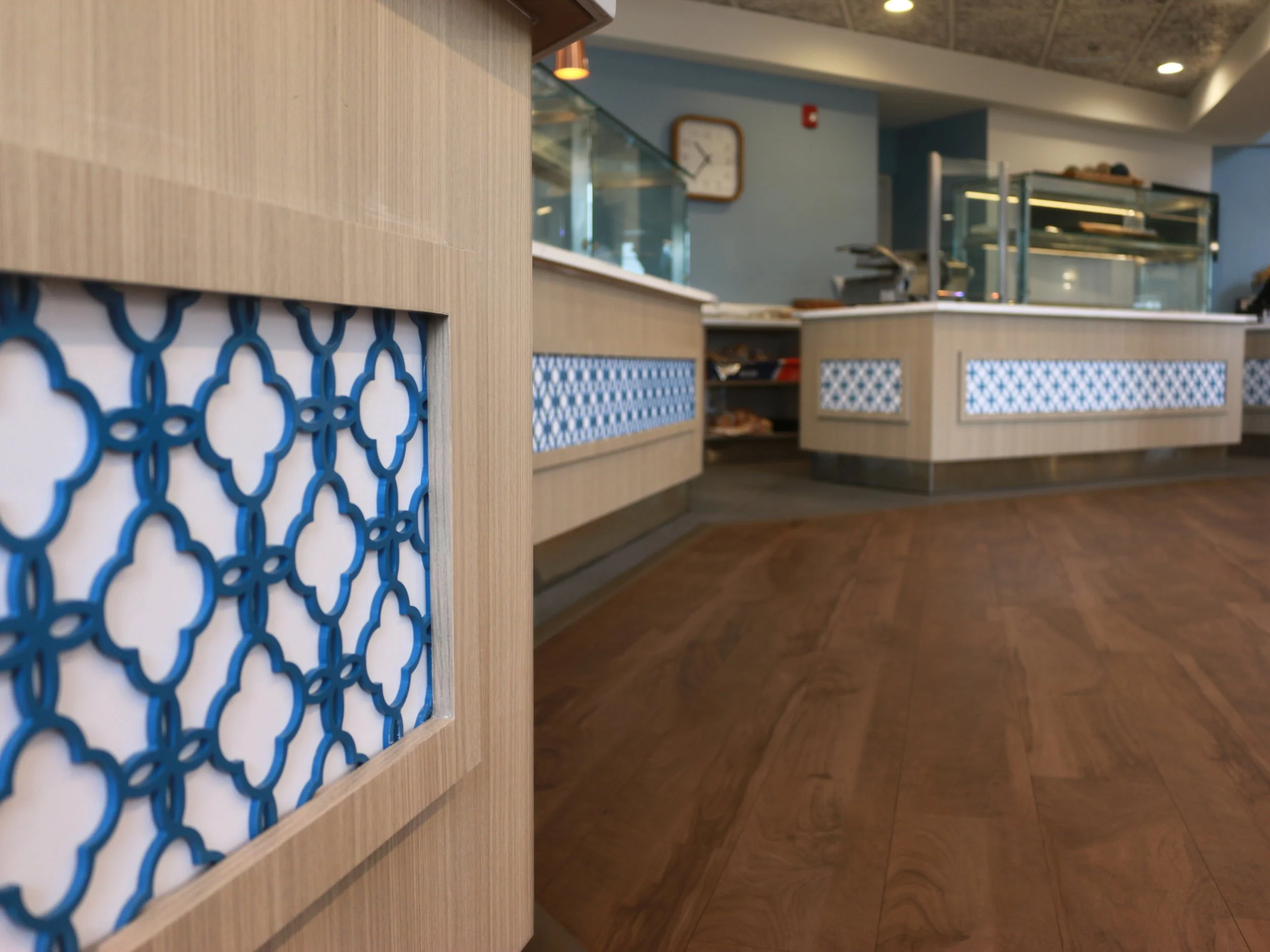 Close-up of a decorative wooden panel with a blue geometric pattern in a restaurant or café, with the background showing a counter and display case.