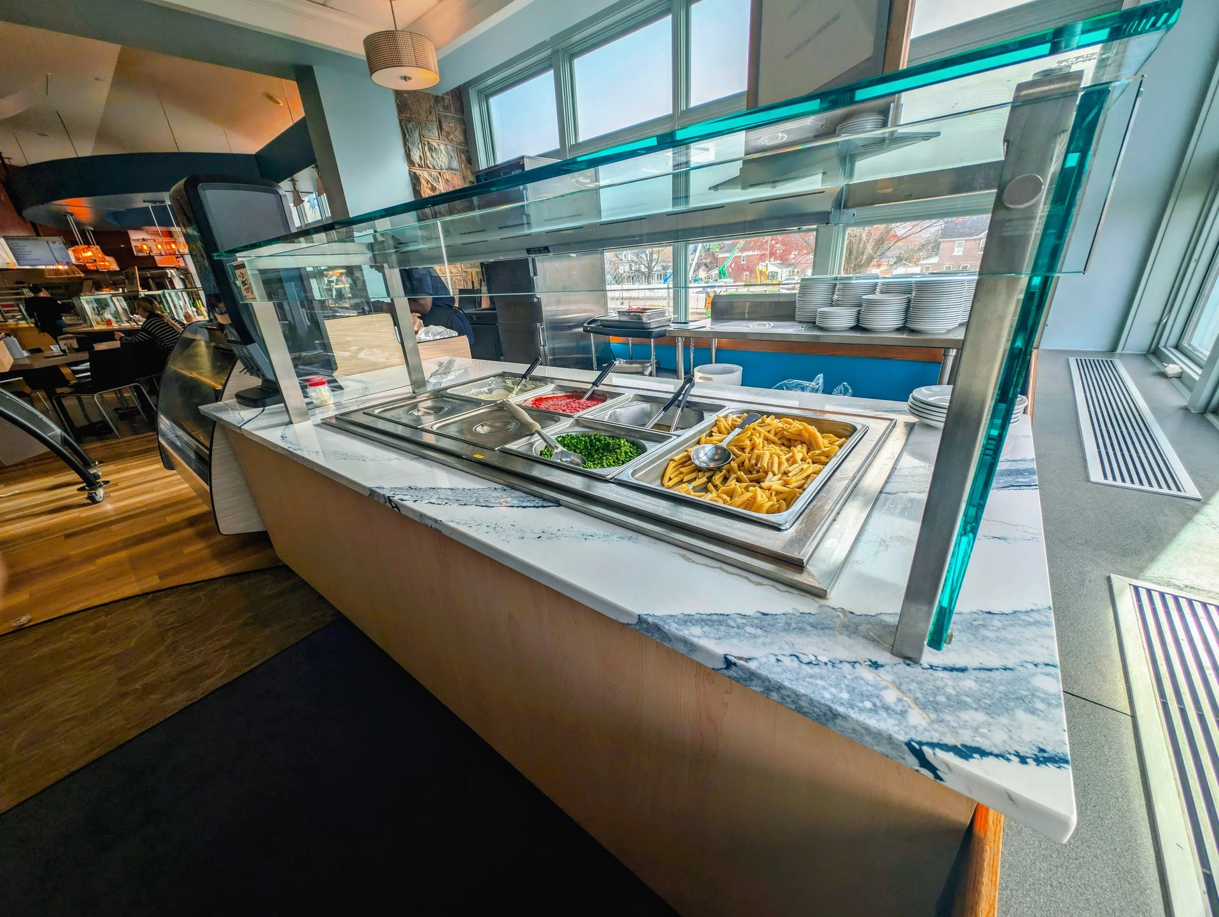 Buffet station with pasta, green onions, diced tomatoes, and other toppings inside a restaurant.