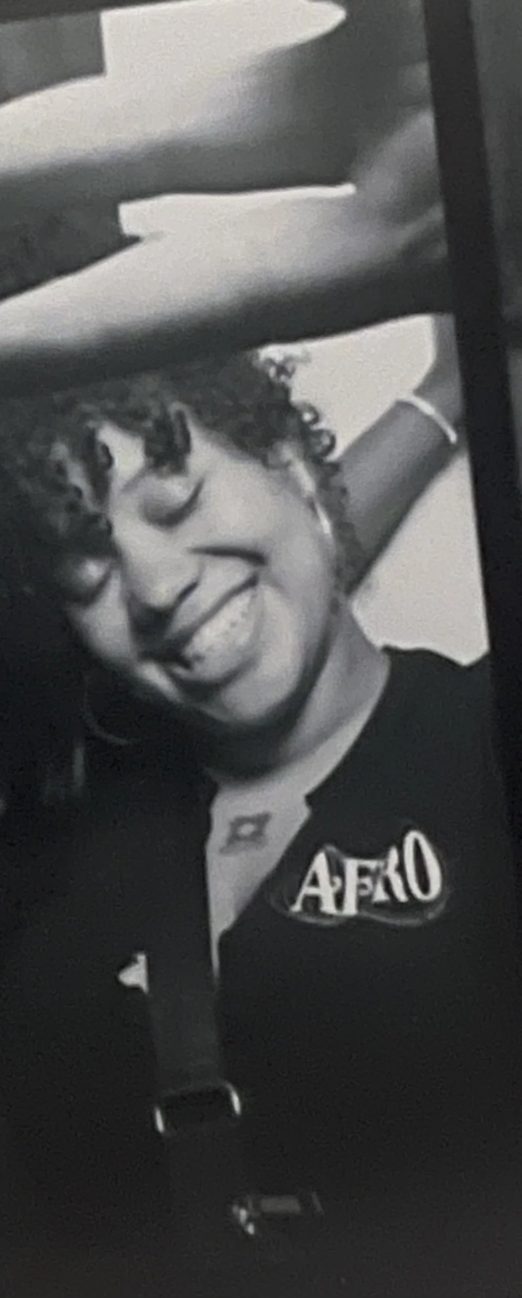 Black and white photo of a woman with curly hair smiling,  wearing a shirt with 'AFRO' written on it.