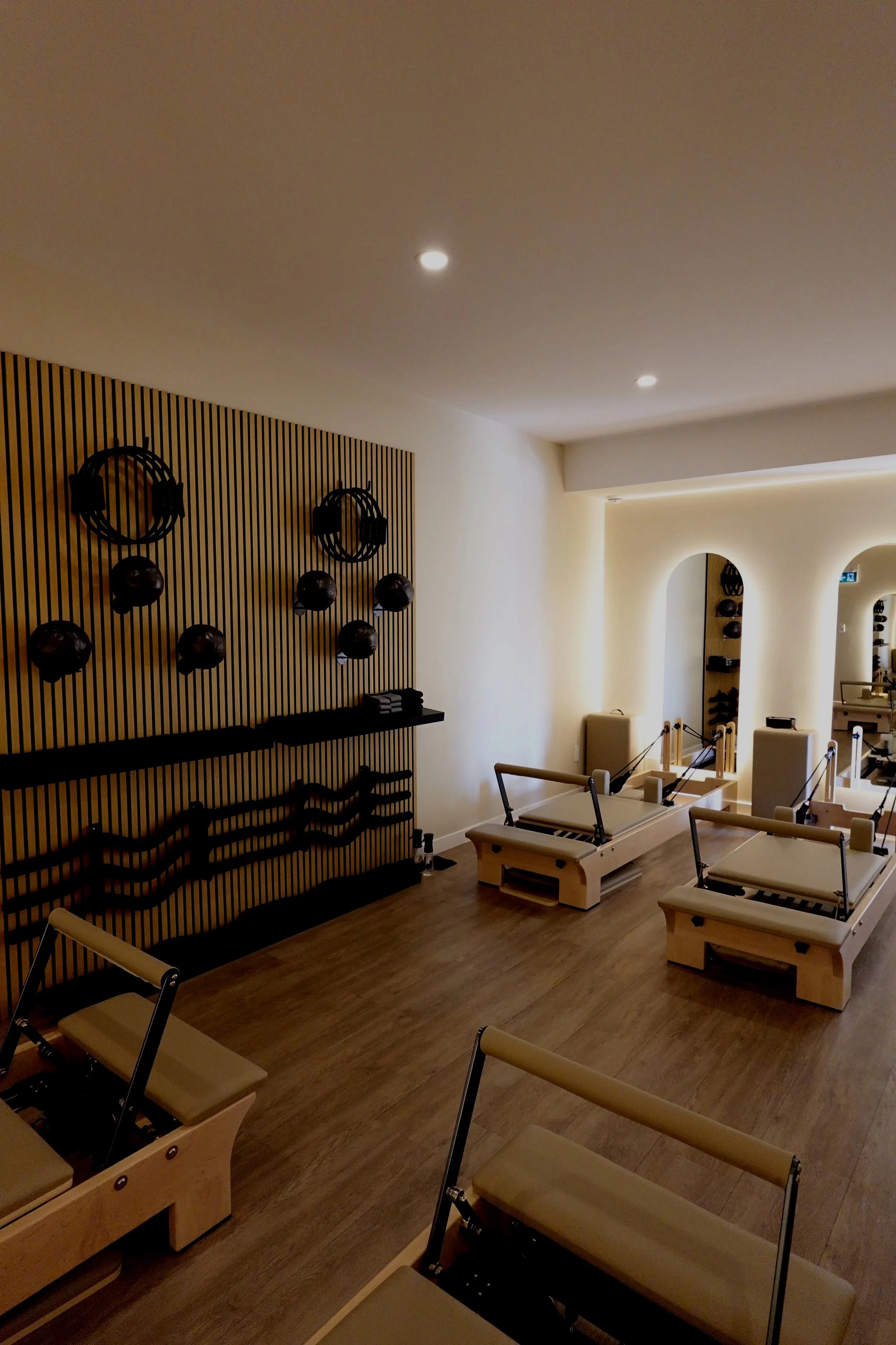 A wellness or massage room with three treatment beds, some fitness equipment on the wall, and warm lighting creating a calming environment.