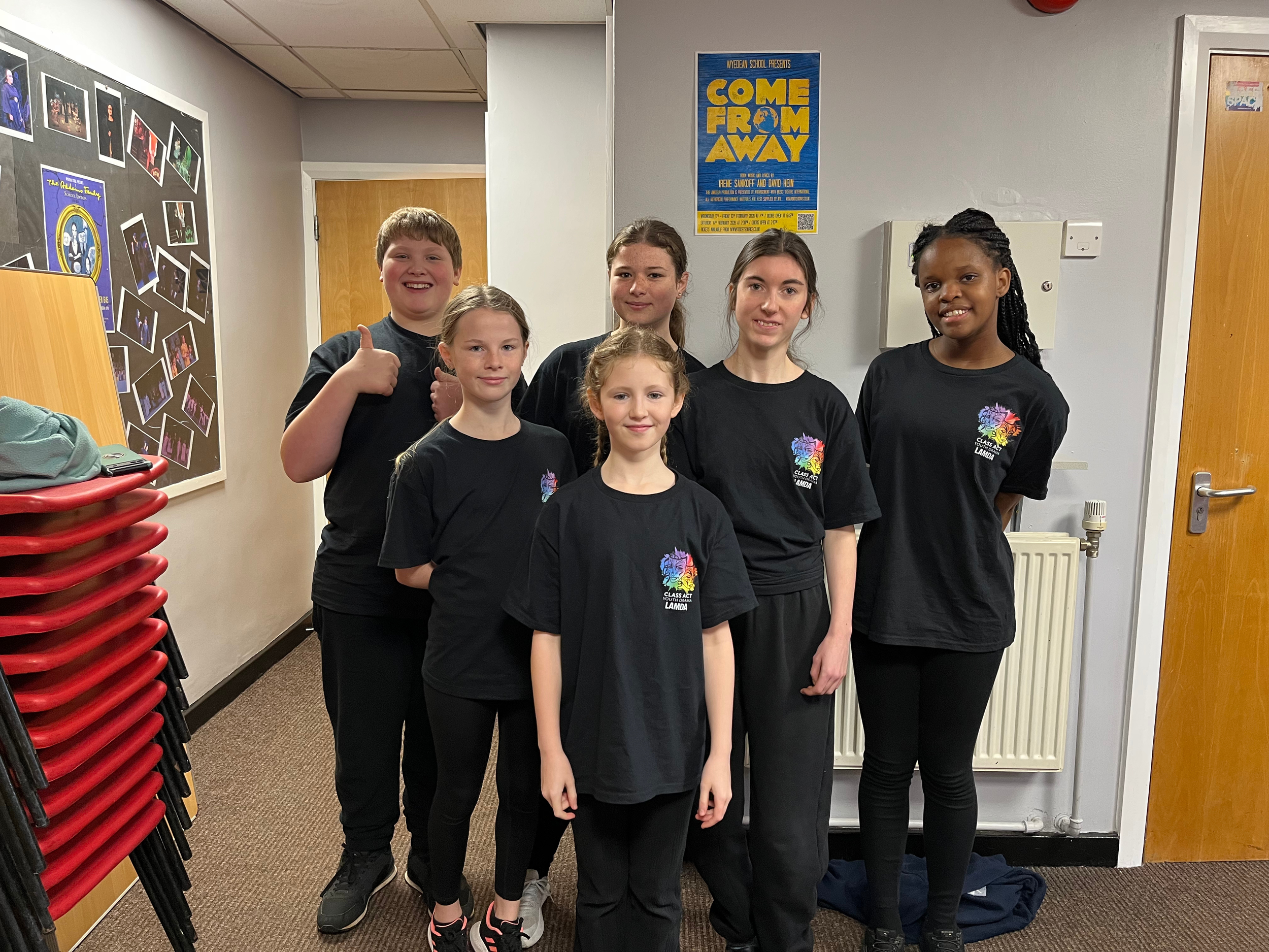 Six children in black t-shirts standing in a hallway, smiling and posing for a photo.