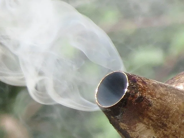 Close-up of the burning end of a smoking pipe with smoke rising from it.