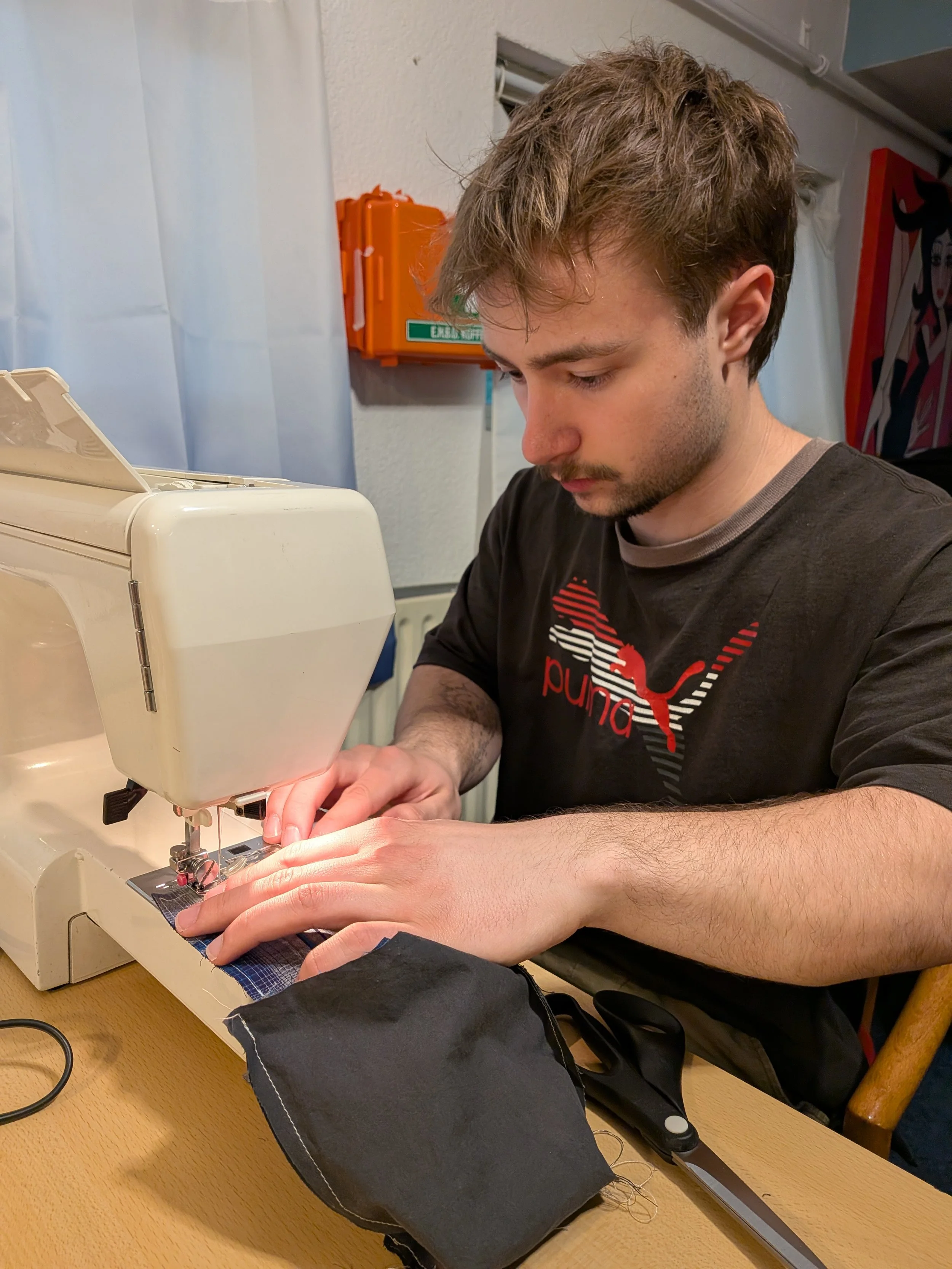 Man die een naaimachine bedient op tafel met een stuk zwart textiel en een schaar.