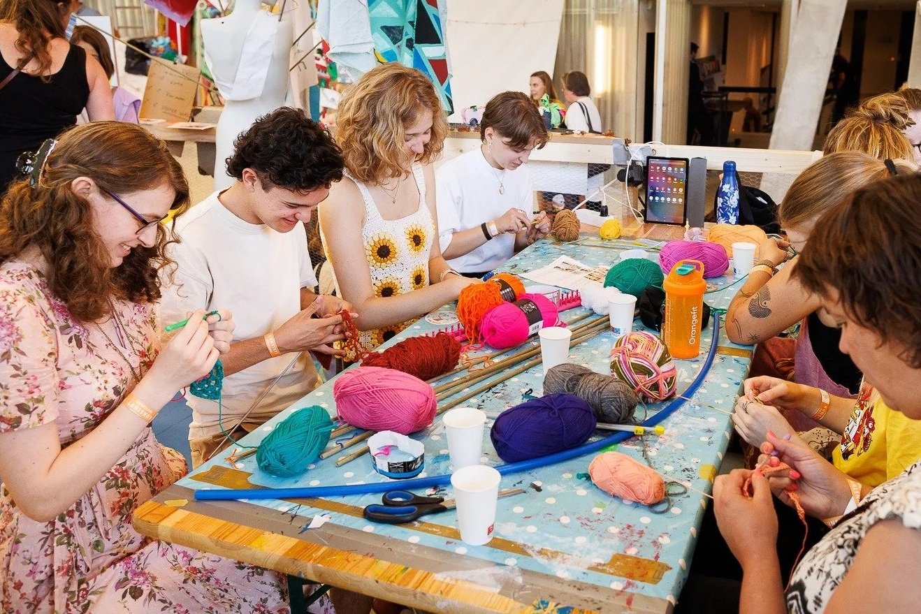 Mensen die samen aan een tafel breien met verschillende gekleurde wol, in een creatieve en gezellige omgeving.