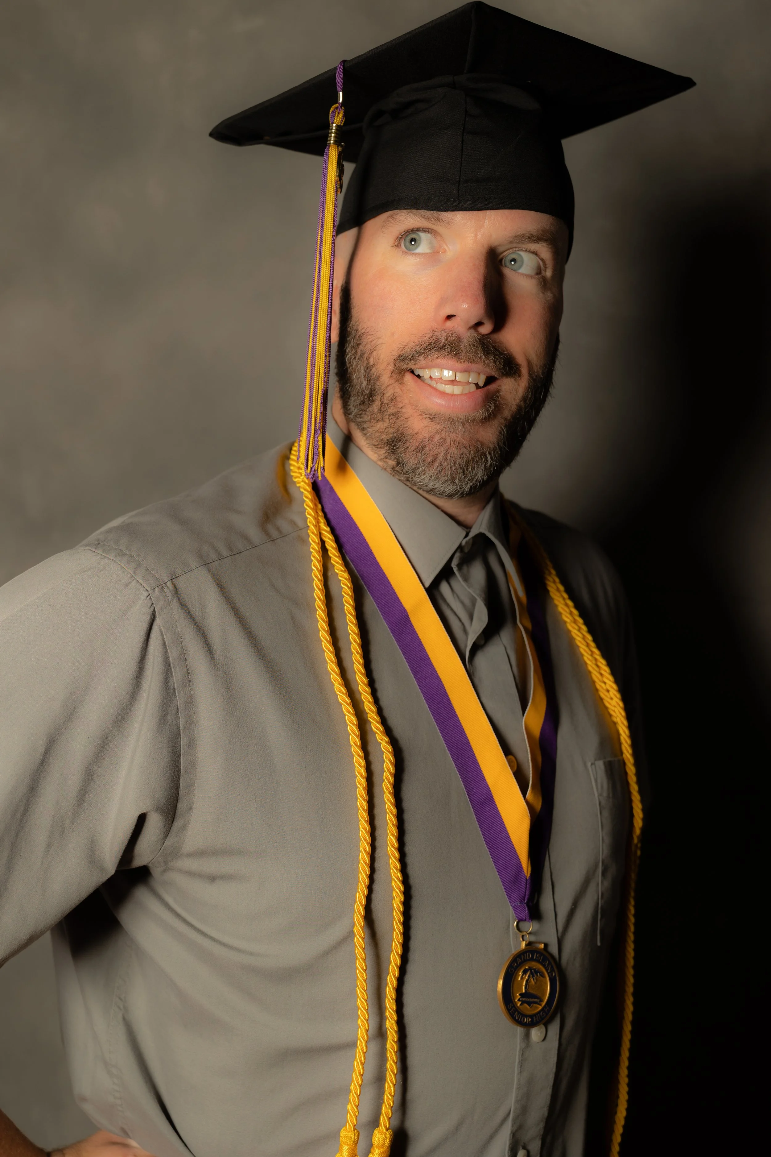 A man in a graduation cap and gown, wearing honor cords and a medal.
