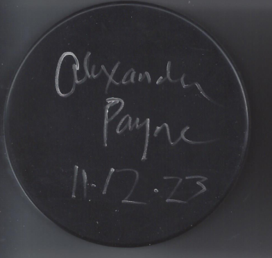 A black circular object with handwritten text in white chalk that reads 'Alexandra Payne 11-12-73'.