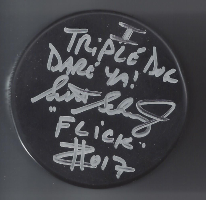 A black hockey puck with handwritten silver text reading "Tripped, you dance you!" and other words, along with a signature.
