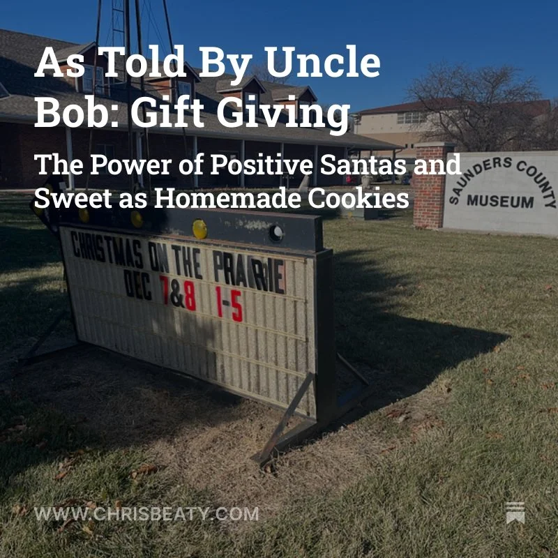 An outdoor sign in front of a building with a gray sign that reads Saunders County Museum at the entrance. The sign below displays the date DEC 7 & 8 and the time 1-5. There is a board on the left with black, red, and yellow colors, but the content is not fully clear.