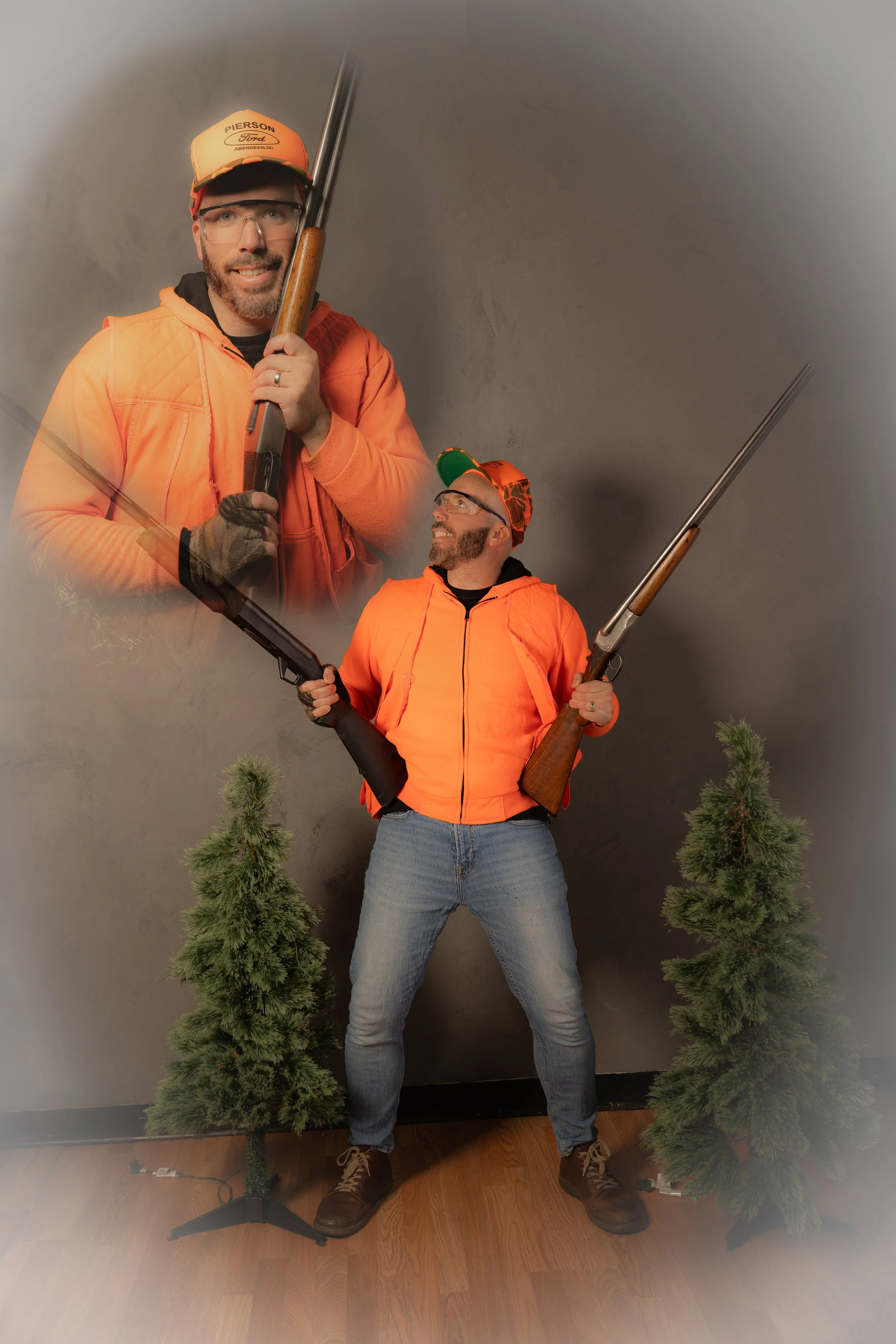 A man in a bright orange jacket and jeans standing with two rifles, one in each hand, against a gray background with small artificial pine trees at his feet. A large, semi-transparent image of another man in similar attire, also holding rifles, appea
