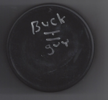 A black circular object with handwritten white text that reads 'Buck' and a mathematical division symbol.