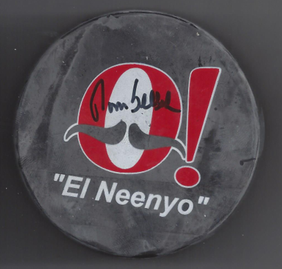 A gray, round object with a red and white logo and text that reads "El Neenyo" and an exclamation point, with handwritten signatures on the logo.