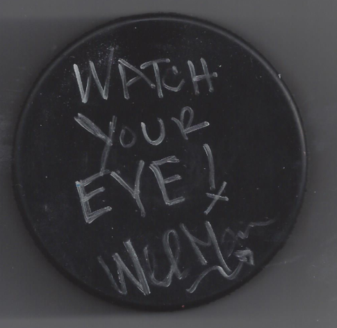 A round black object, possibly a lid or sign, with the handwritten message 'WATCH YOUR EYE!' in white chalk or marker.