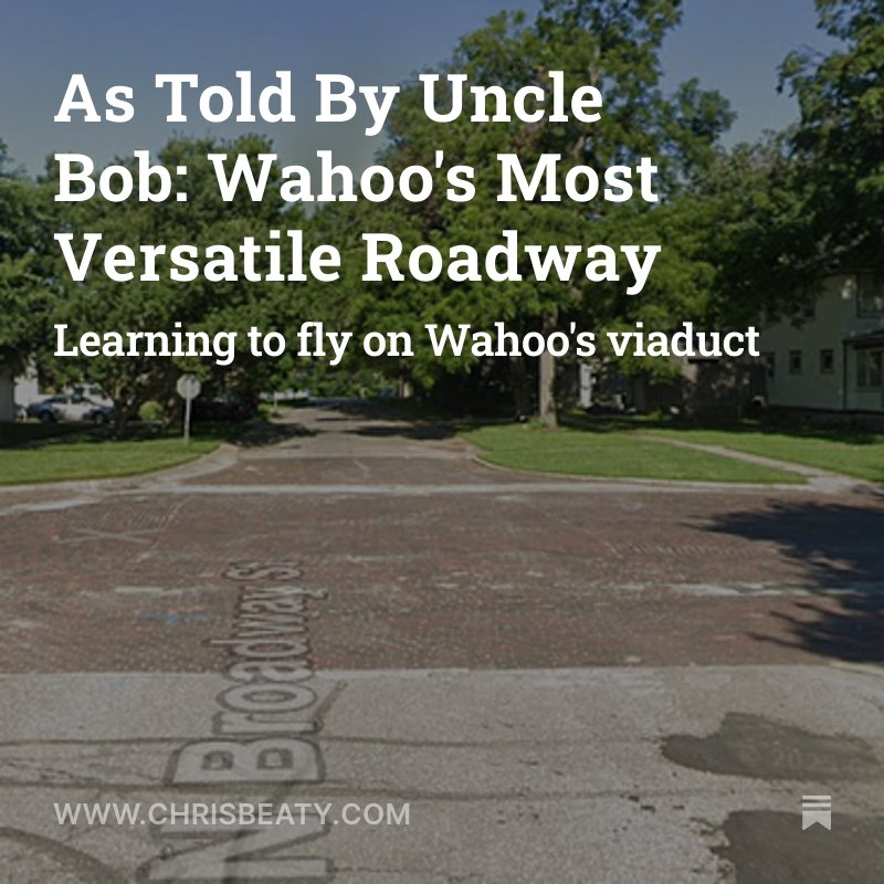 Photo of a brick-paved street with white painted text reading 'Wahoo' and 'Roadway' on the pavement. Green trees and houses are in the background.