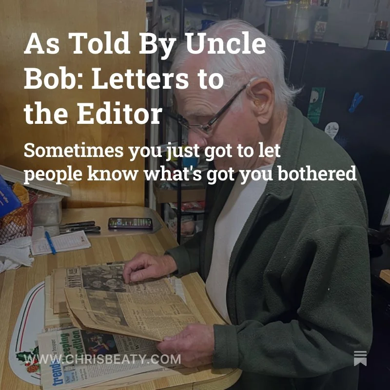 An older man with gray hair and glasses is reading a newspaper at a desk surrounded by various office supplies.