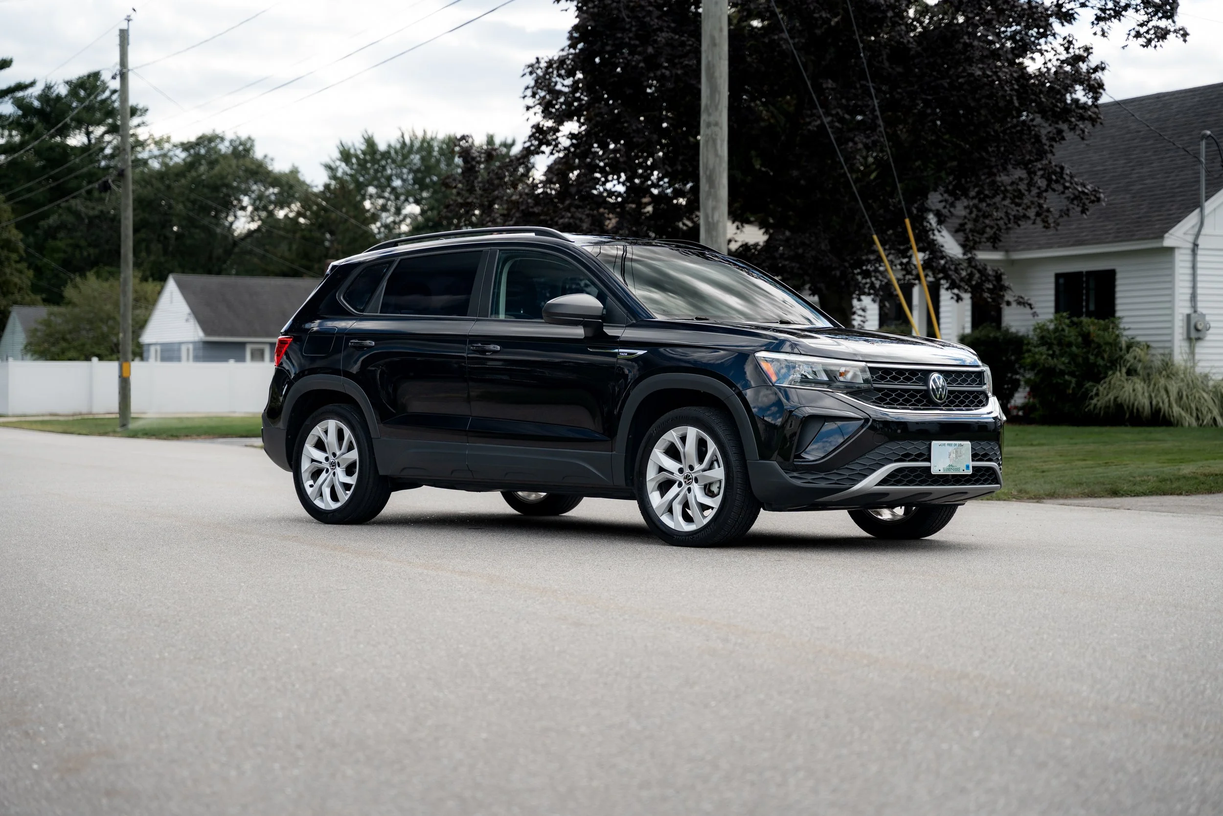 A black Volkswagen SUV parked on a suburban street with houses and trees in the background.