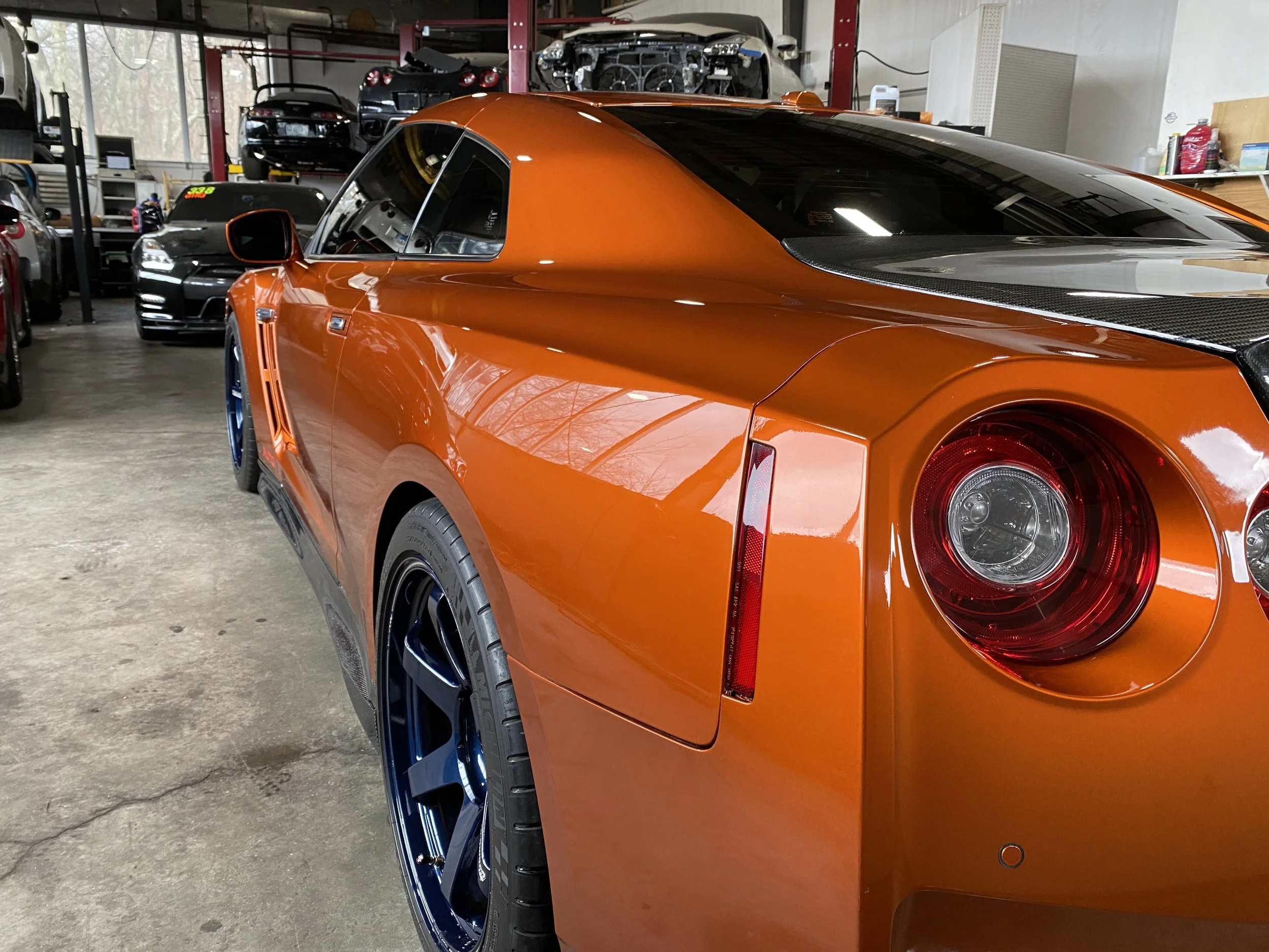 Orange sports car inside a garage, with multiple cars stored on shelves in the background.
