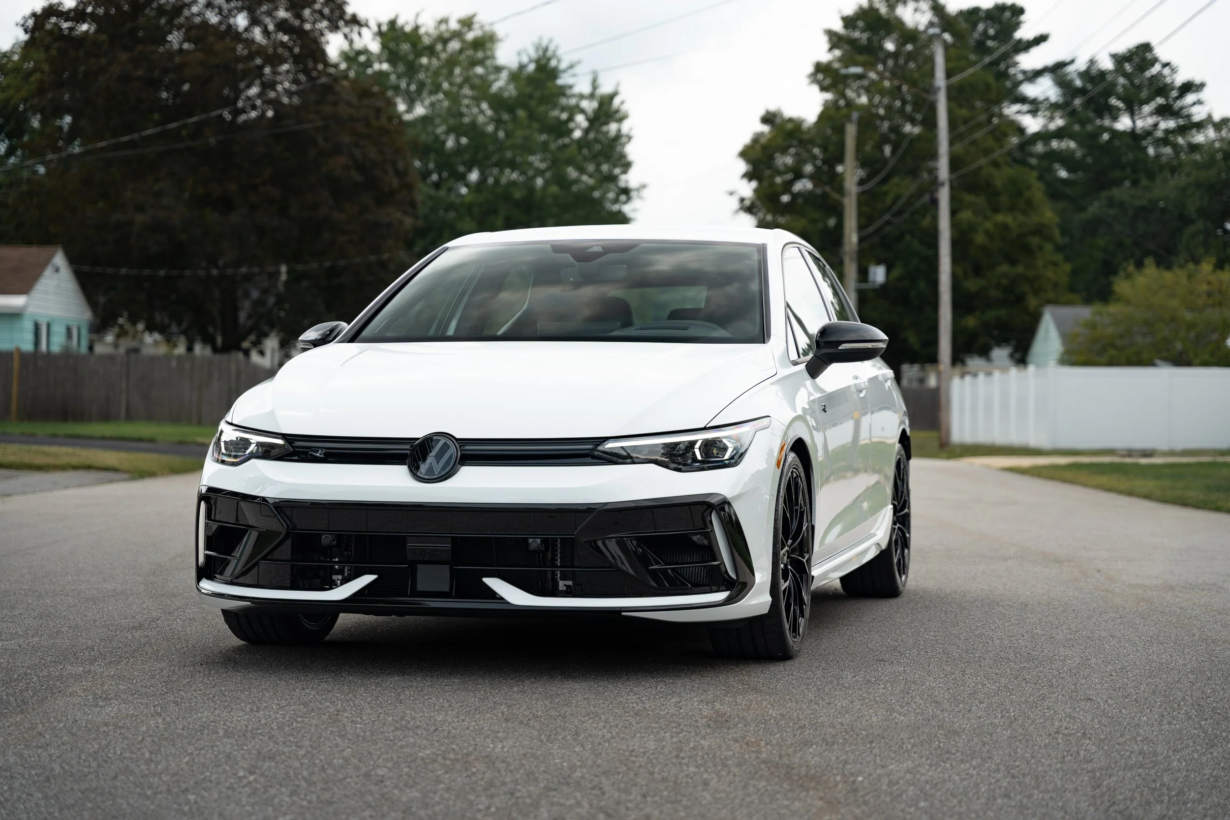 A white Volkswagen car parked on a suburban street with trees and houses in the background.