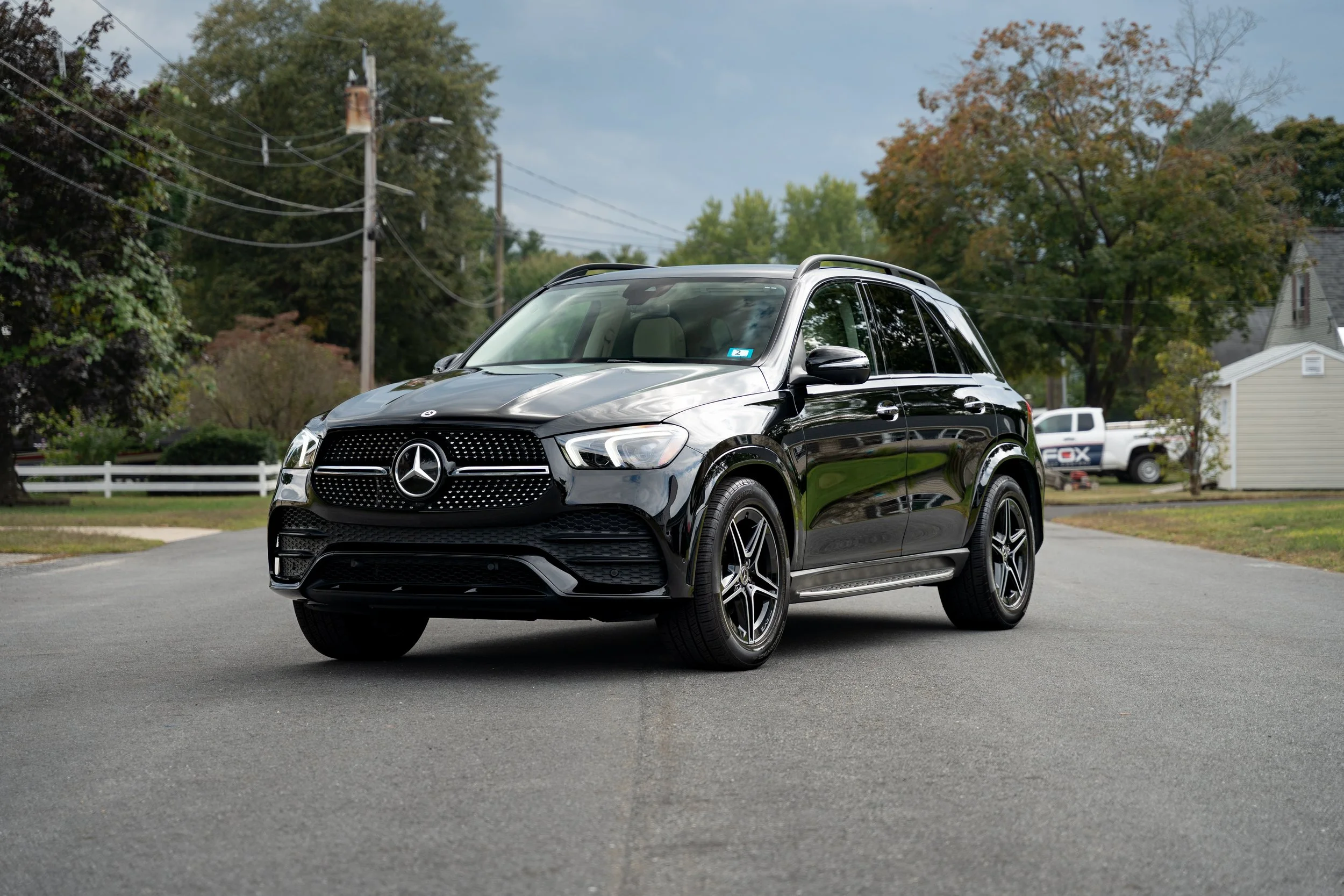 Black Mercedes-Benz SUV parked on a residential street with trees, houses, and utility poles in the background.