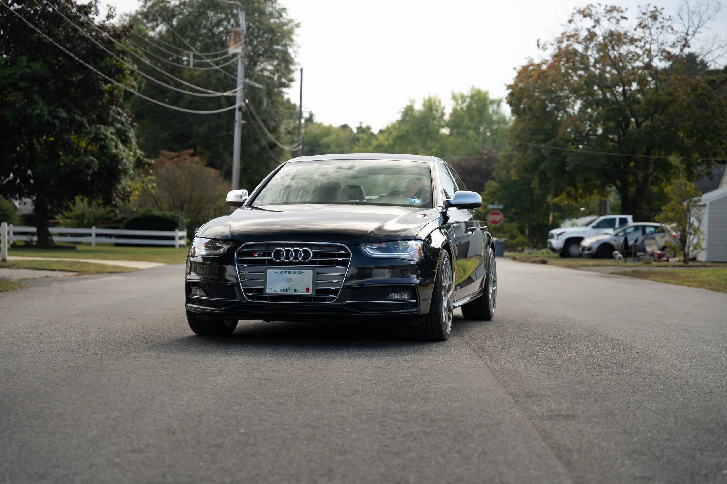 A black Audi sedan parked on a suburban street with trees and houses in the background.