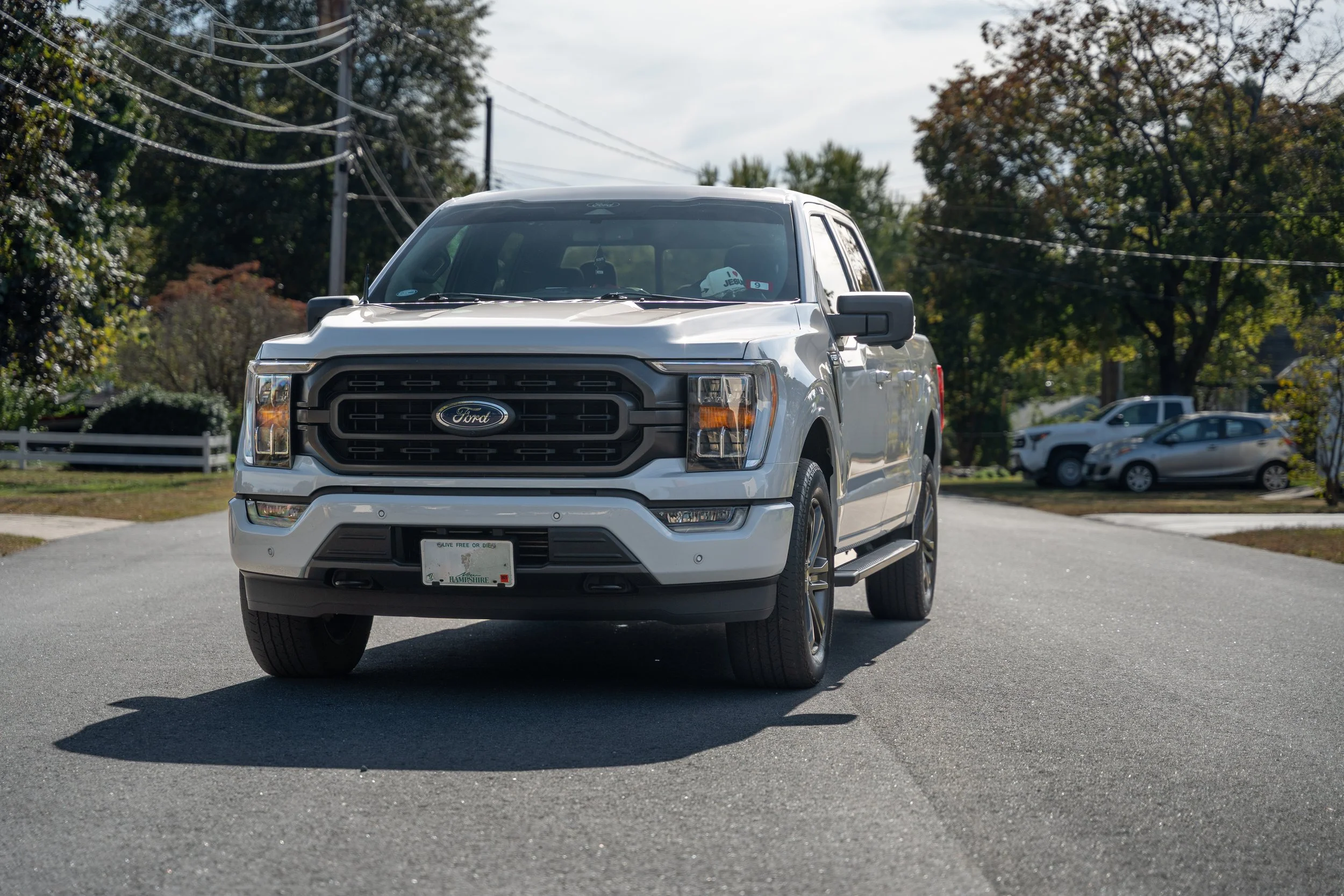 A white Ford pickup truck parked on a residential street with trees and other vehicles in the background.