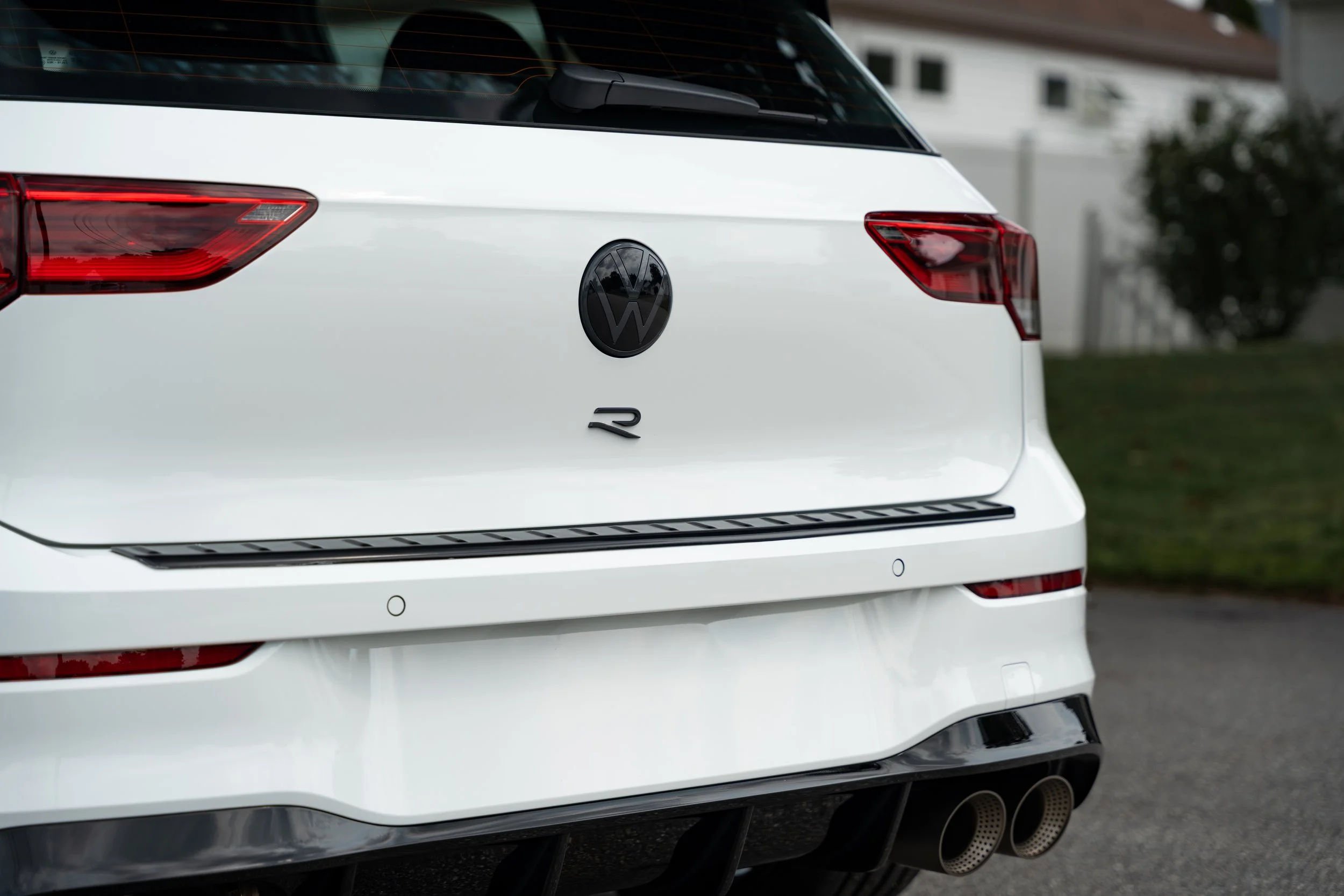Rear view of a white Volkswagen R vehicle on the street, showing the VW logo, taillights, and dual exhaust pipes.