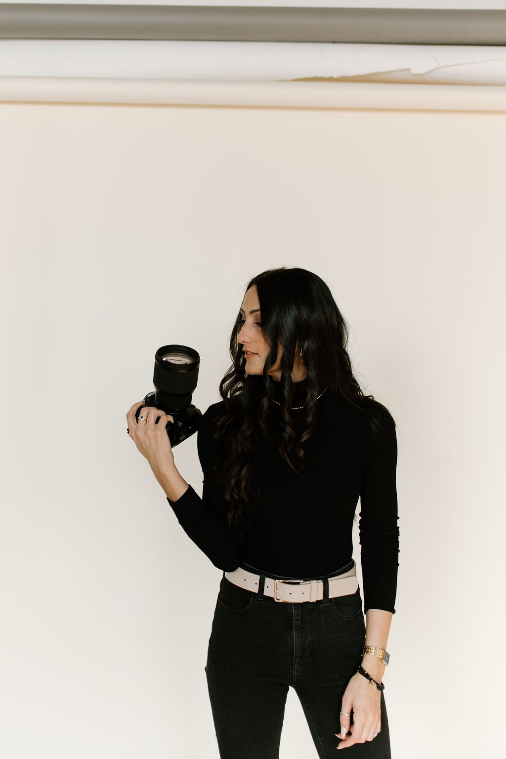 A photo of Julia Brown standing in the center looking to the left at her camera in front of a white wall background.