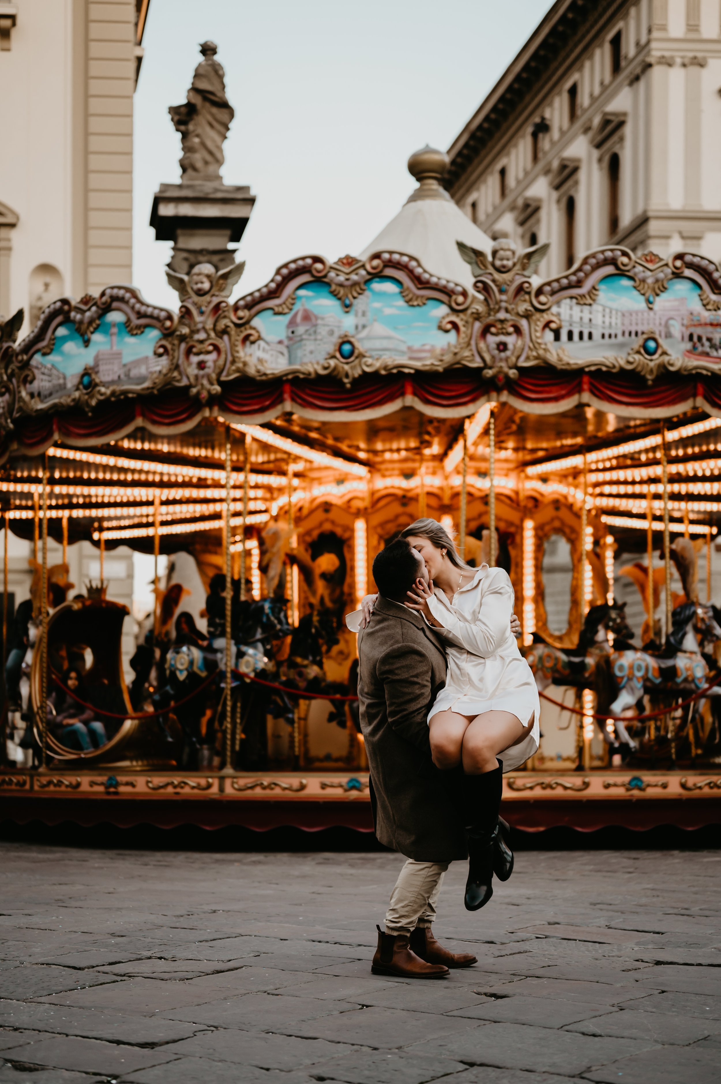 A photo of a husband holding his wife in front of a carousel in the middle of Florence Italy