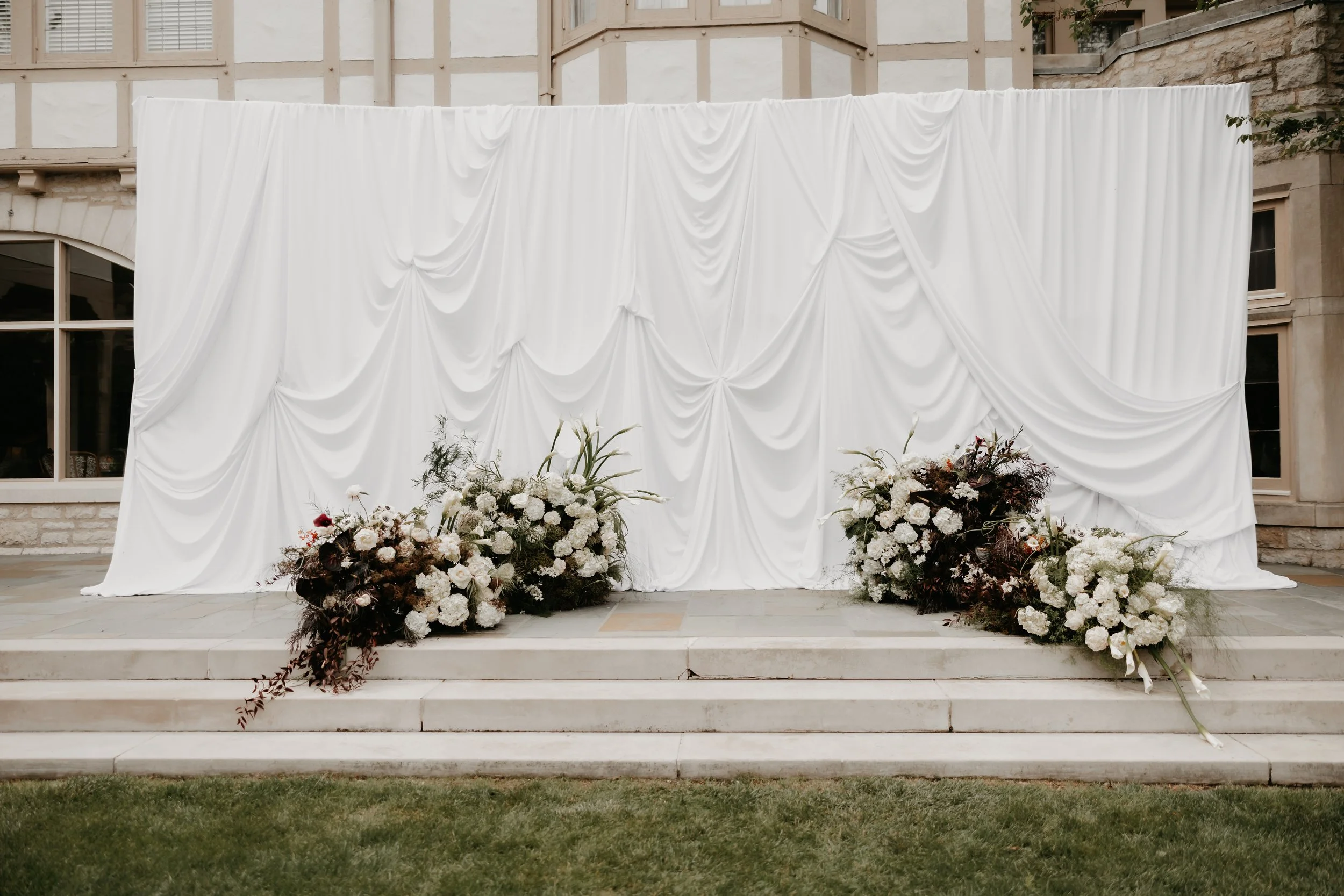 Modern white draping and organic floral installations creating an editorial outdoor wedding ceremony backdrop, photographed by Julia Brown Photo.