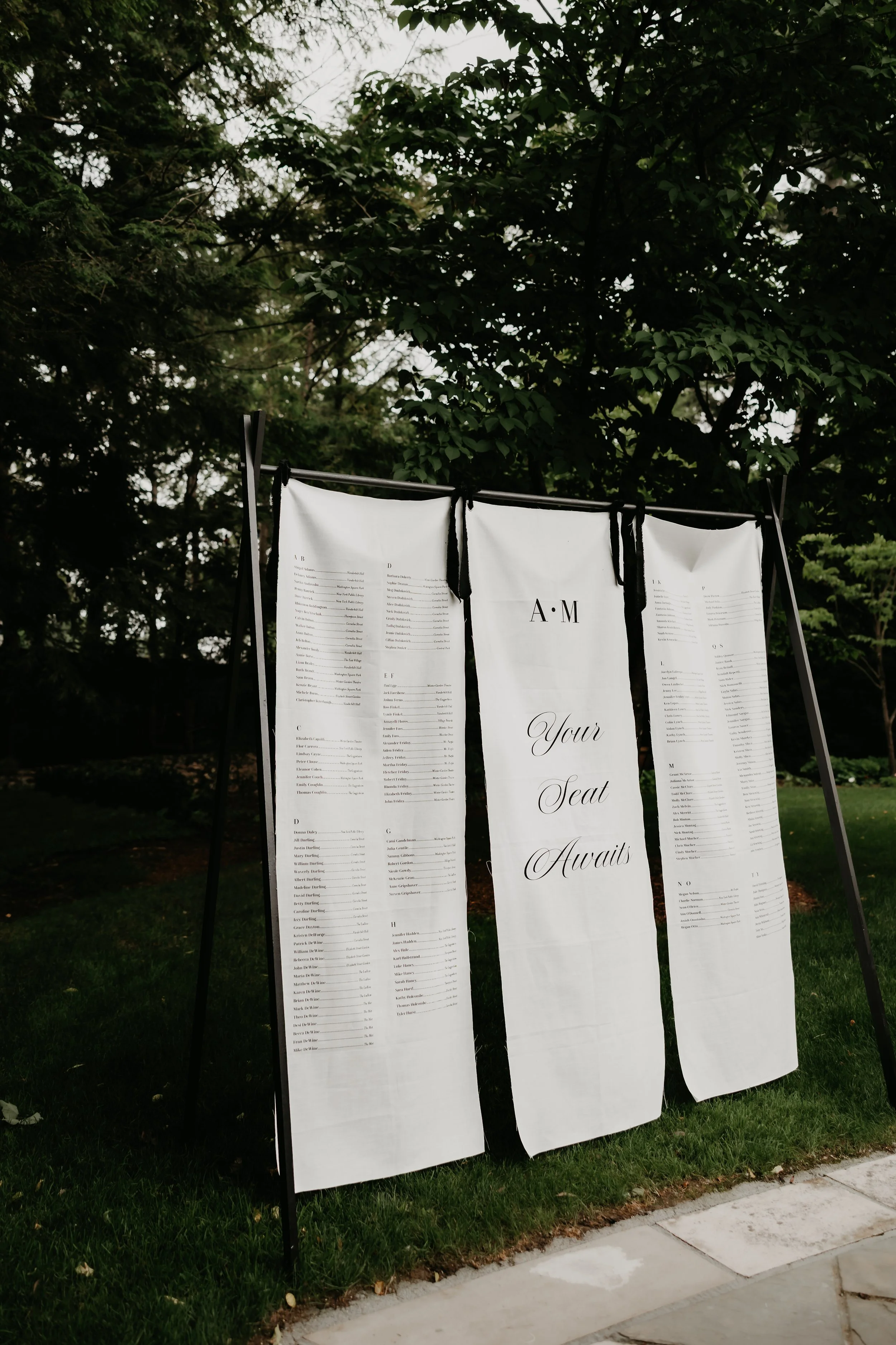 Black-and-white wedding seating chart displayed on linen drapery beneath the trees at the Ohio Governor’s Residence and Heritage Garden, photographed by Julia Brown Photo.