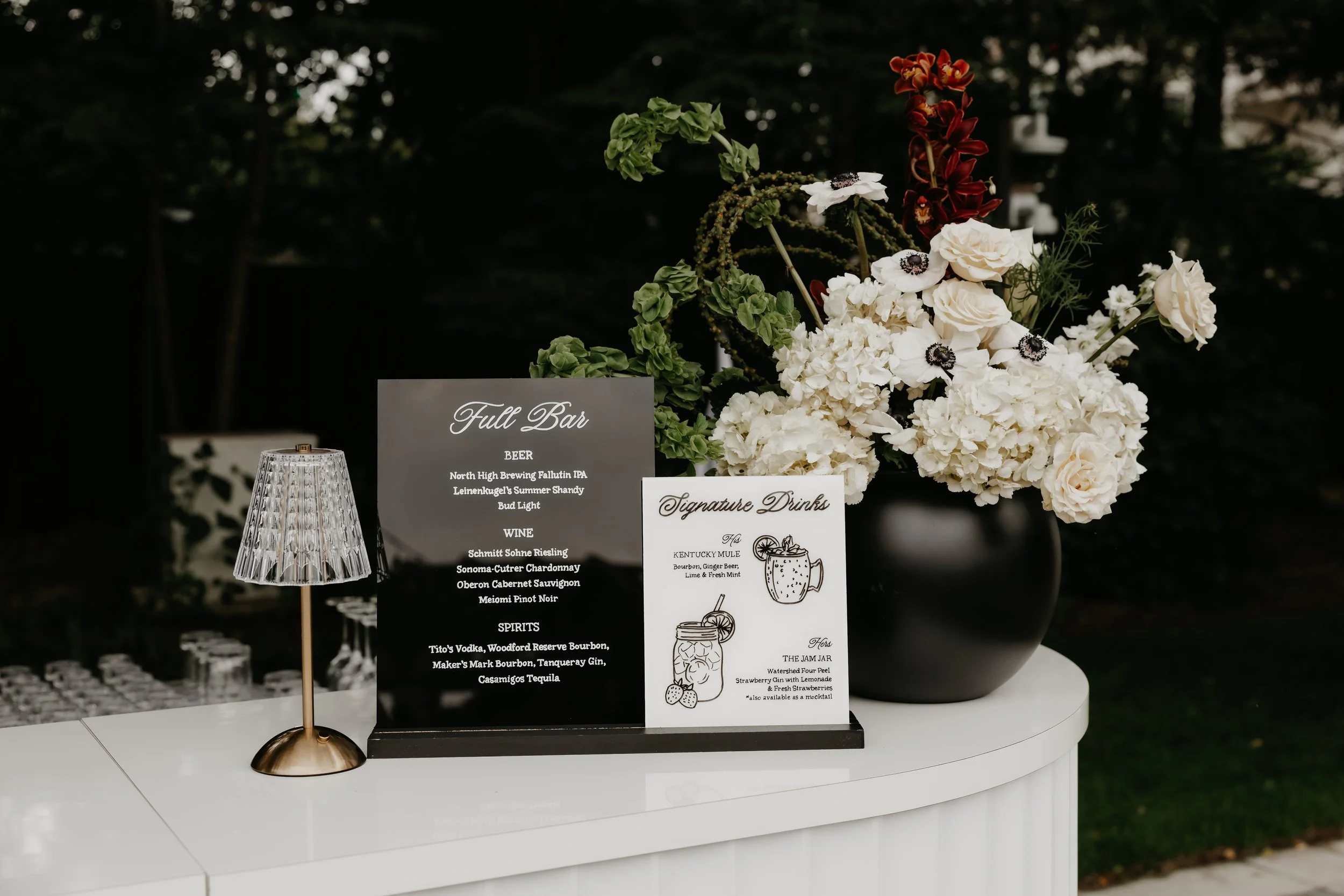 Wedding bar display featuring signature cocktail menus and an organic white floral arrangement, photographed by Julia Brown Photo.