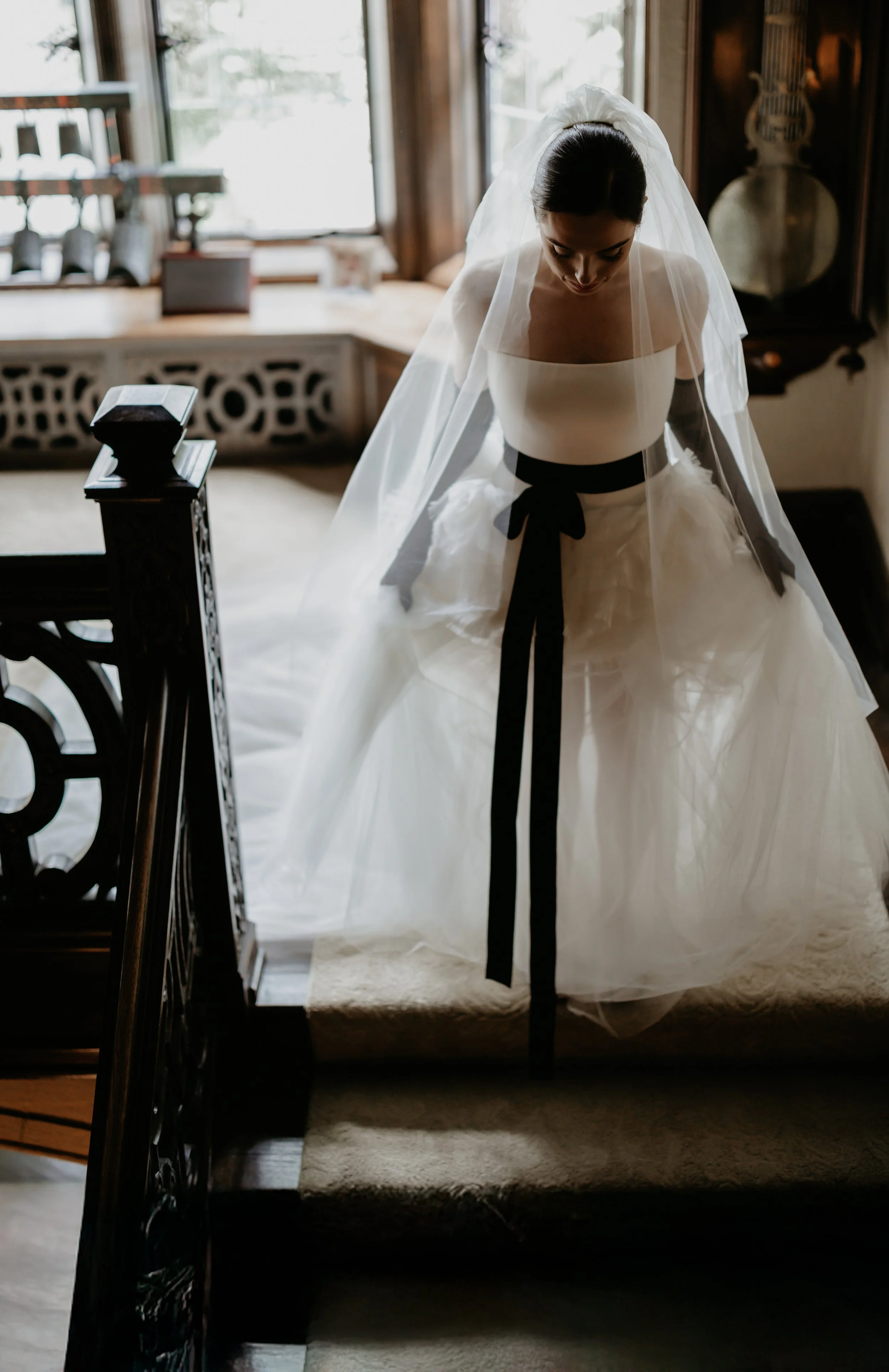 Bride descending the staircase in a Vera Wang wedding gown with a black velvet sash and sheer veil, photographed by Julia Brown Photo.