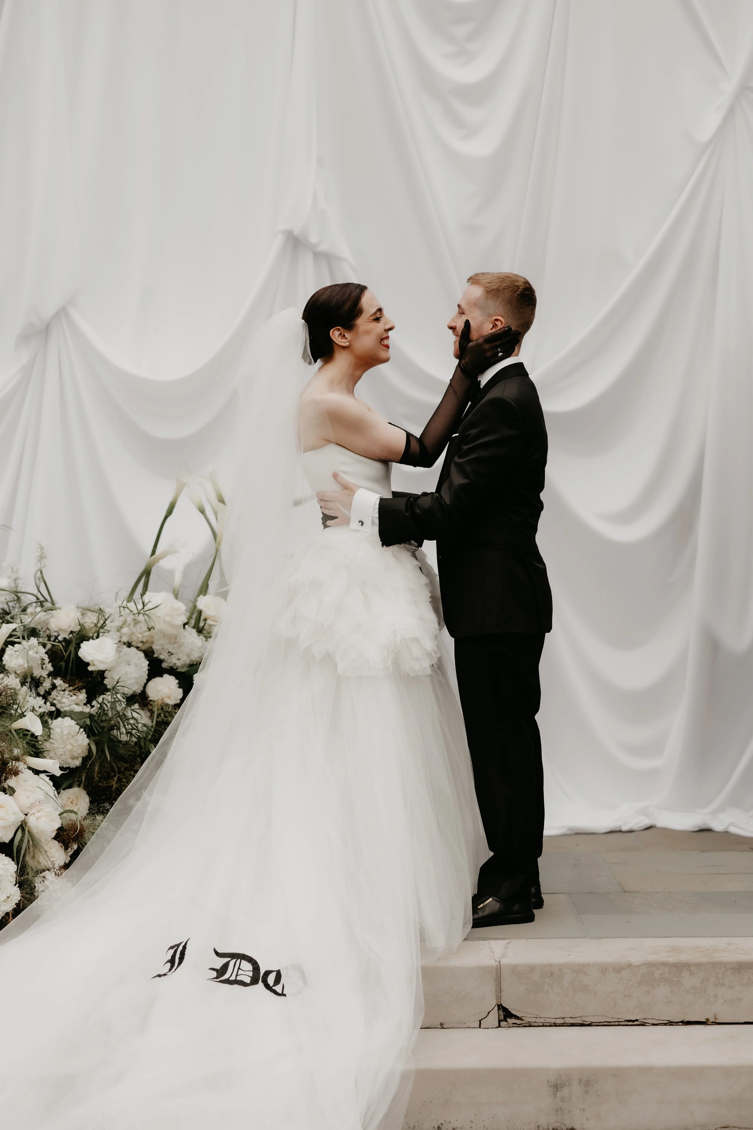 Bride smiling at the groom during their outdoor wedding ceremony against a modern white draped backdrop, photographed by Julia Brown Photo.