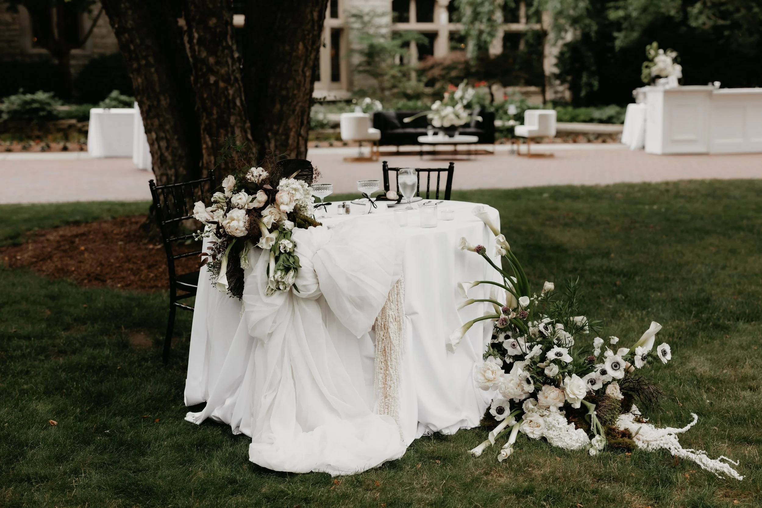 Sweetheart table decorated with layered white linens, a large white draped bow, and organic floral arrangements at the outdoor wedding reception, photographed by Julia Brown Photo.