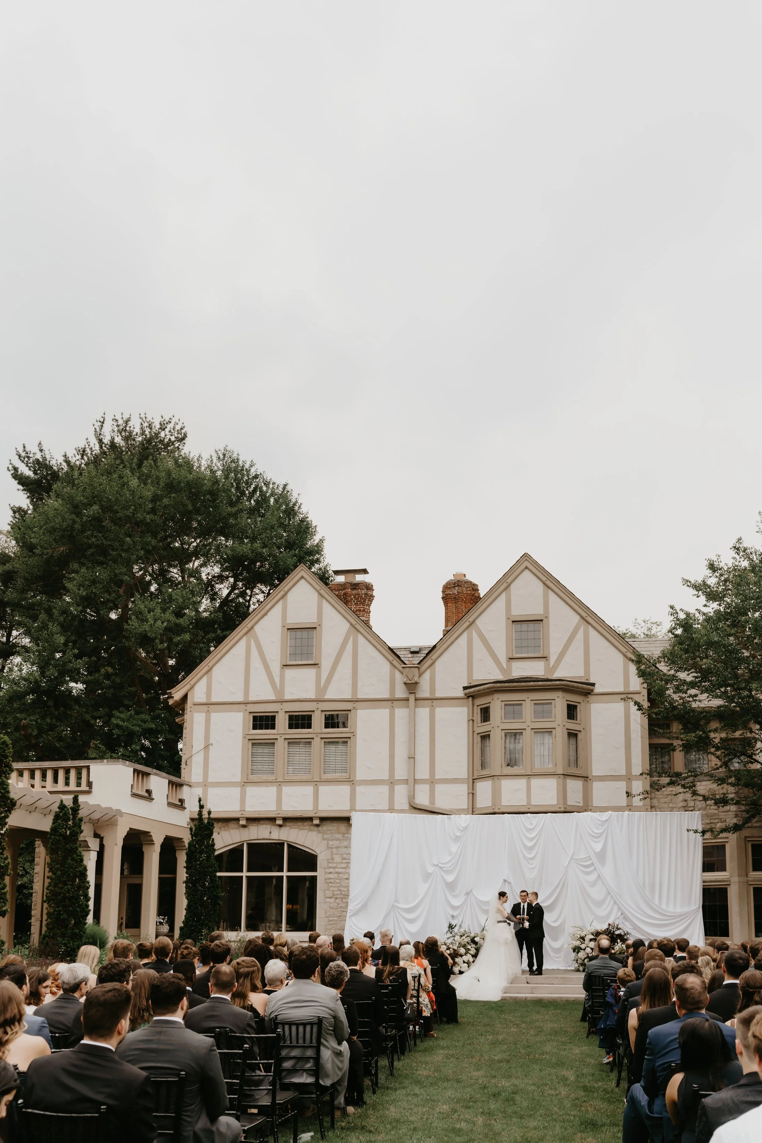 Outdoor wedding ceremony at the Ohio Governor’s Residence and Heritage Garden with guests seated before a white draped backdrop, photographed by Julia Brown Photo.