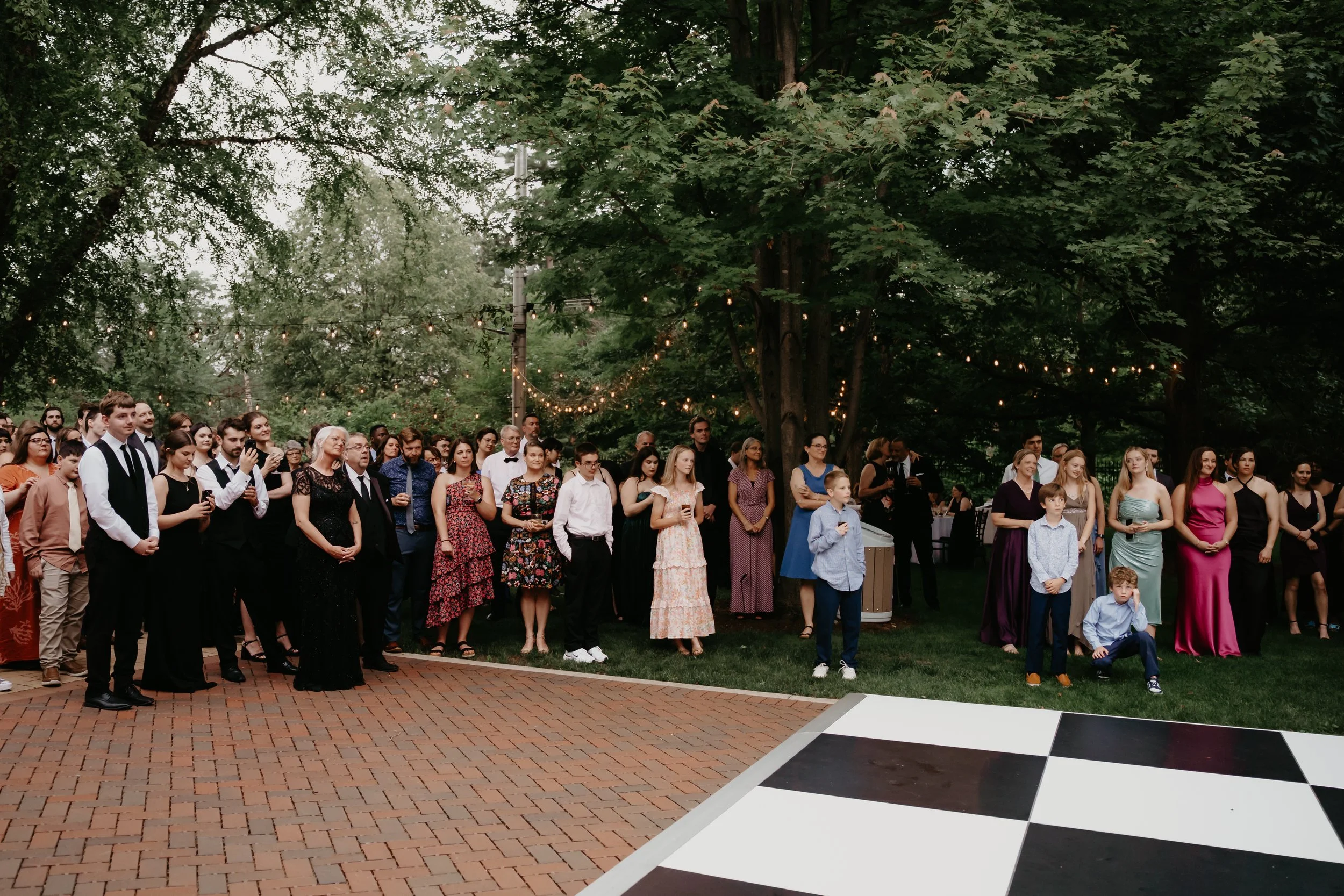 Wedding guests gathered around a black-and-white dance floor beneath string lights in the Heritage Garden, photographed by Julia Brown Photo.