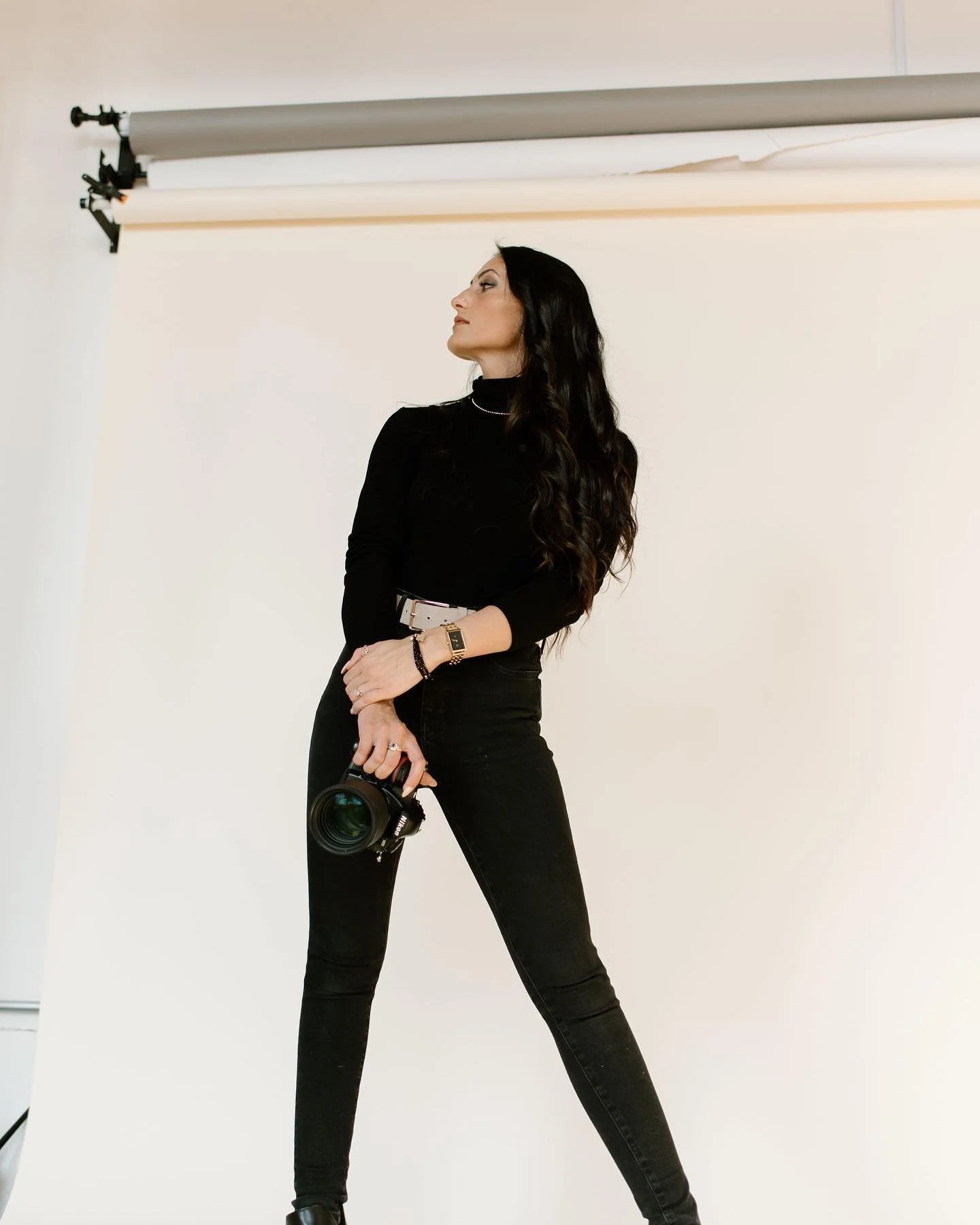 Julia Brown in black clothing holding a professional camera in a photography studio with a white backdrop.