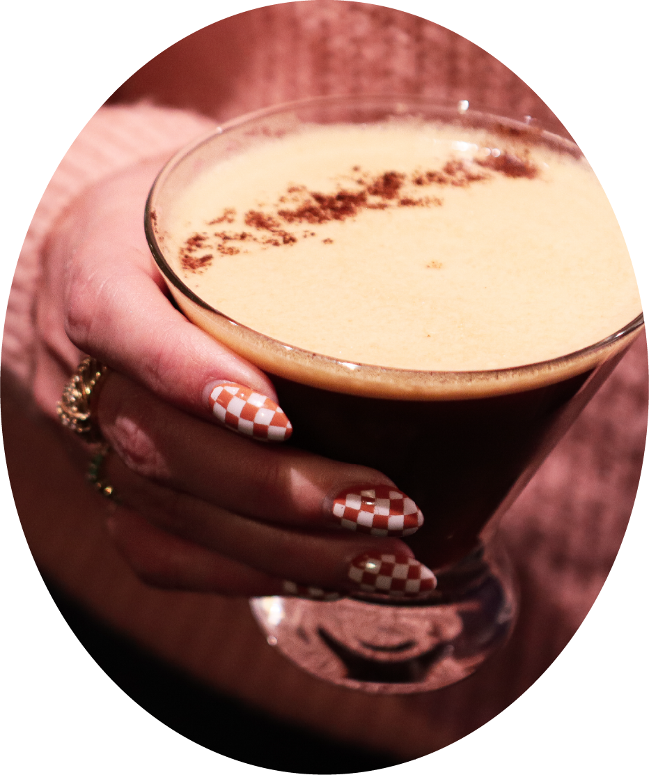 A person holding an espresso martini with a checkered nail design.