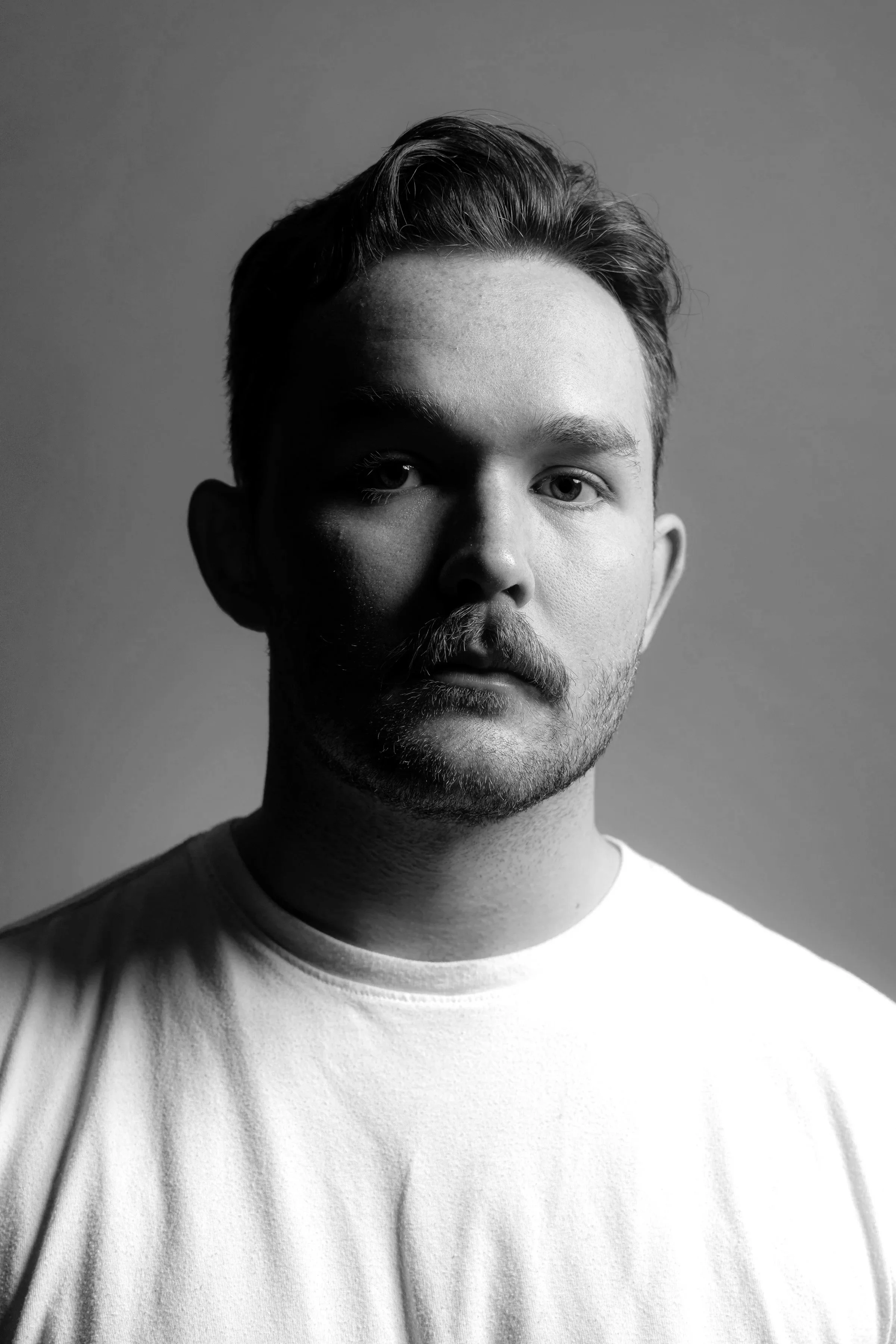 A photo of Owen Taupier wearing a white T-shirt, staring directly at the camera.