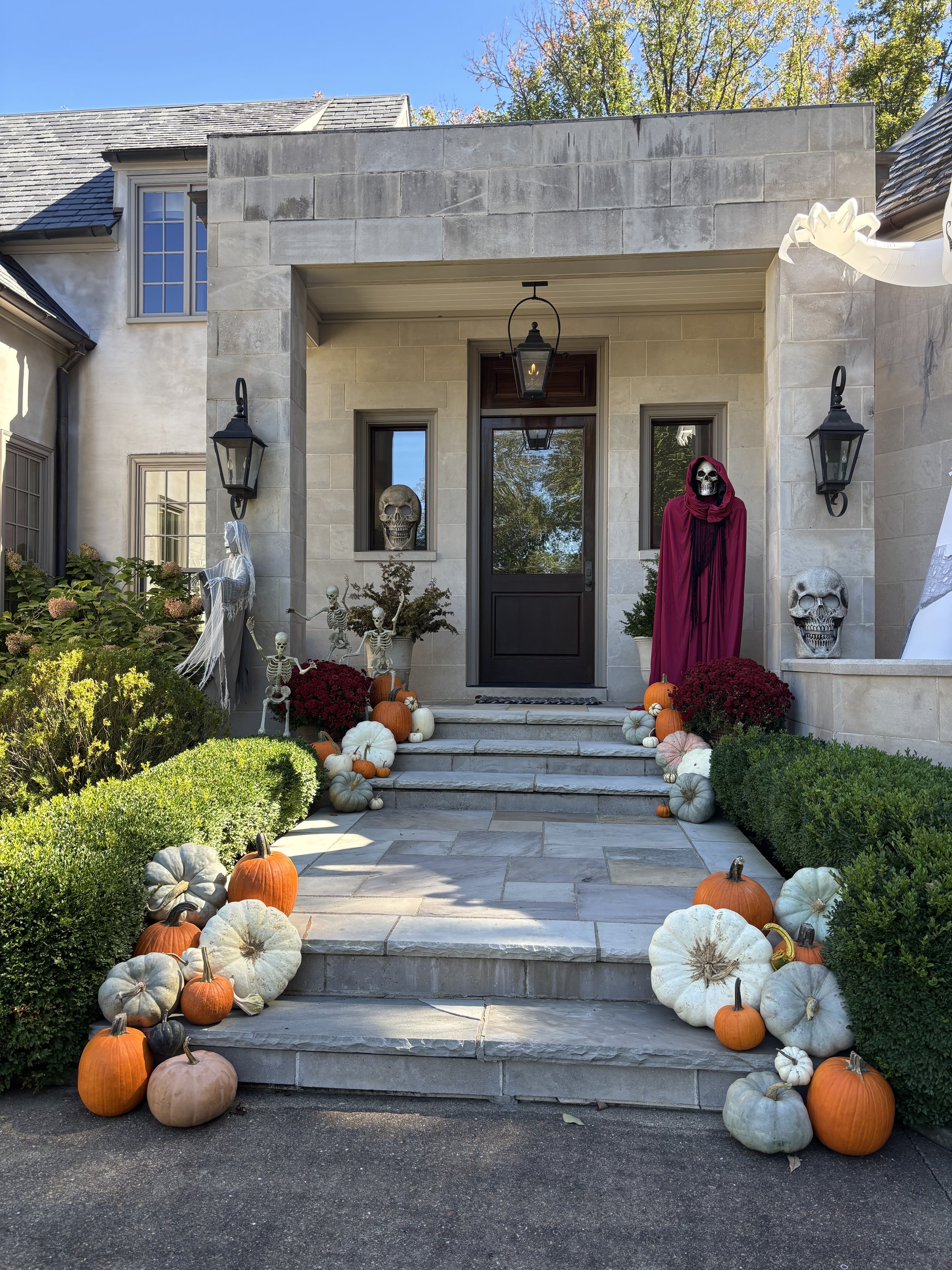 Fall display of pumpkins and gourds on brick steps leading to a porch with a black chair and lanterns.