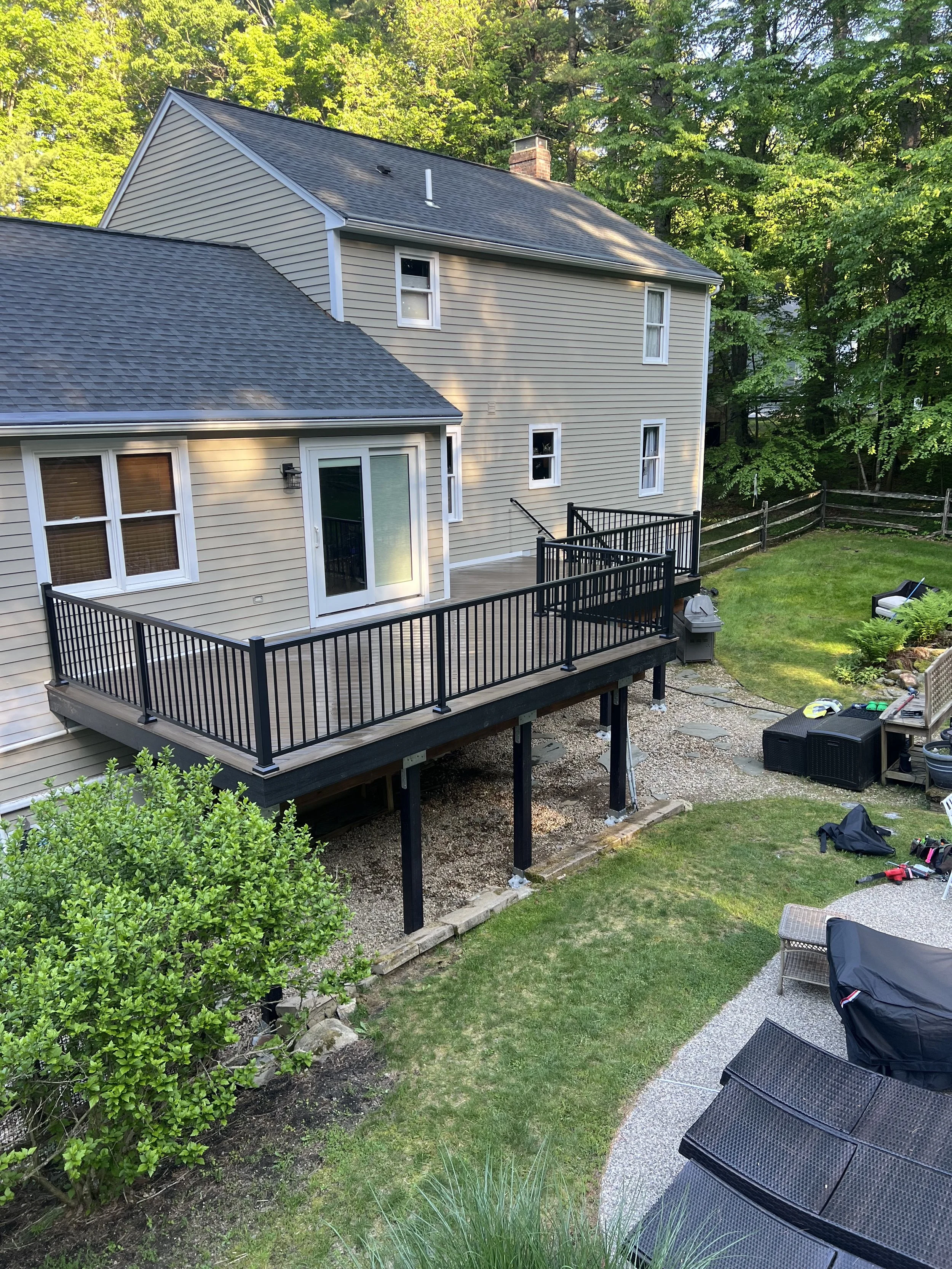 A newly built raised deck attached to a light yellow house with steps leading down to a grassy yard.