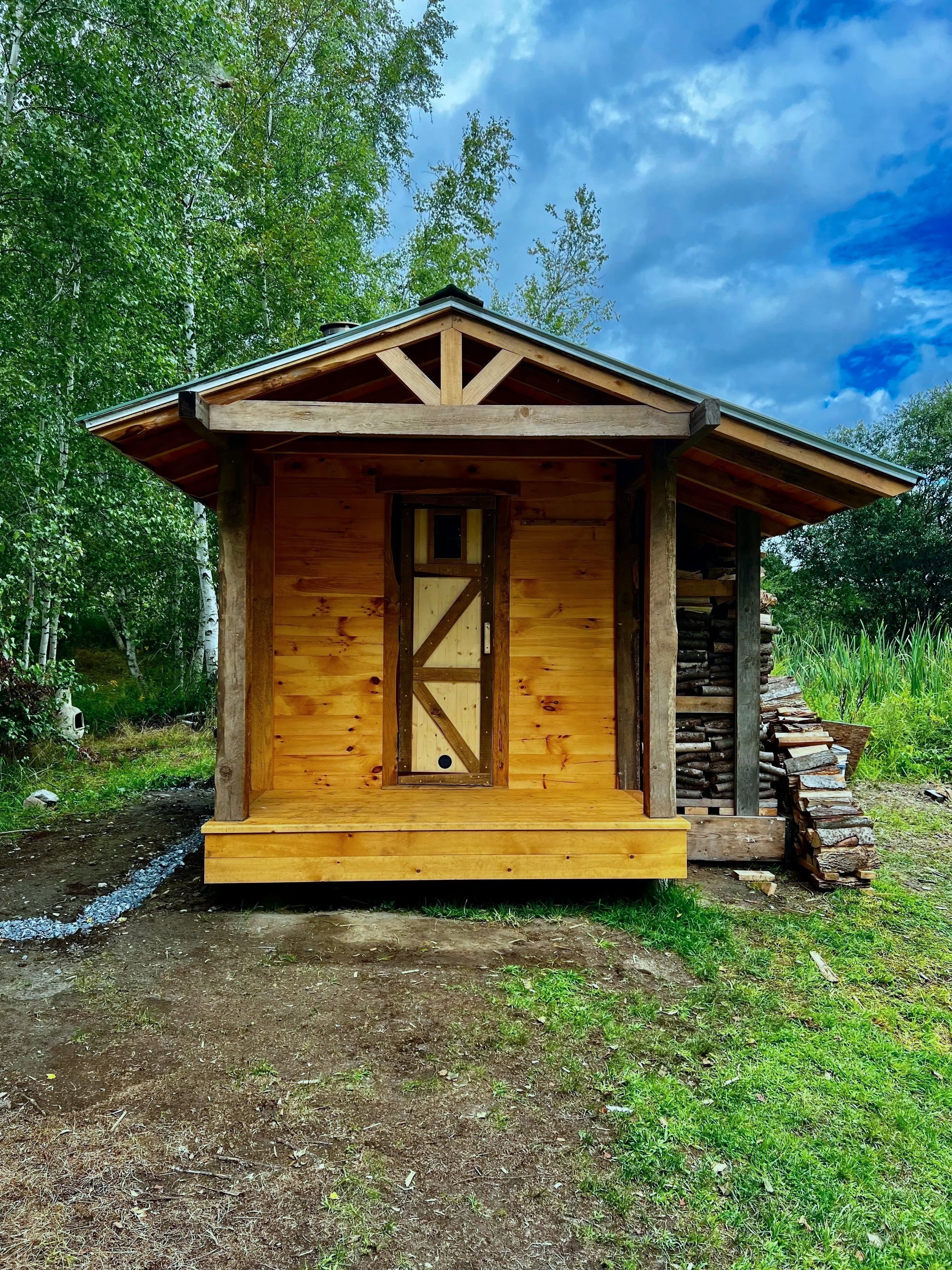 Custom outdoor sauna by Hot Bird Saunas featuring a gable roof, front entry door, and integrated side storage for firewood.